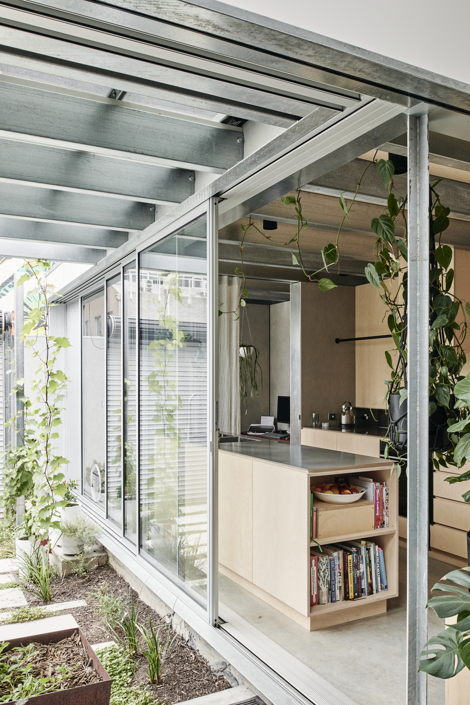 Kitchen island under exposed steel beams with climbing vines framing the glazed courtyard beyond