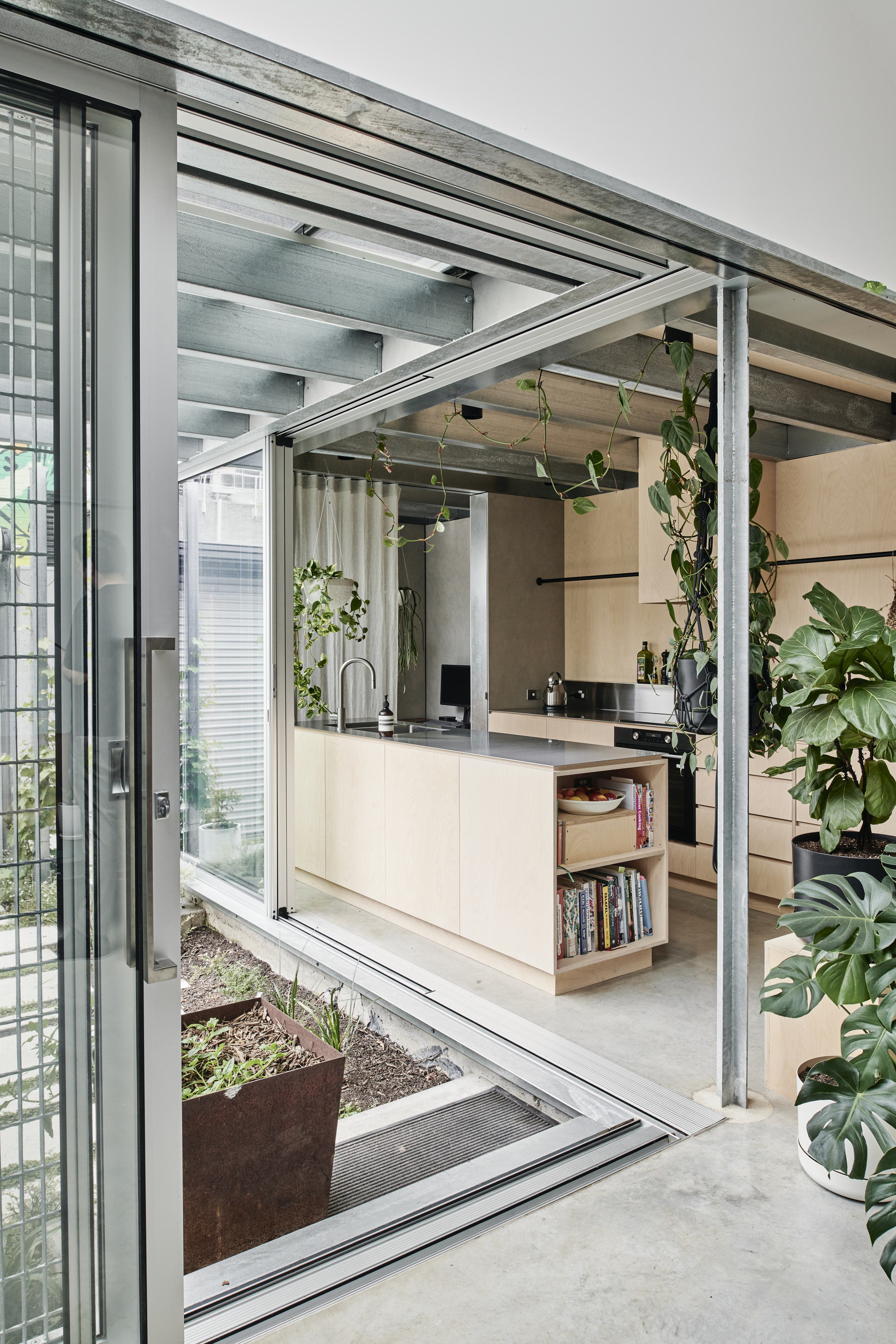 Open sliding glass doors revealing the kitchen and steel structural frame with hanging plants