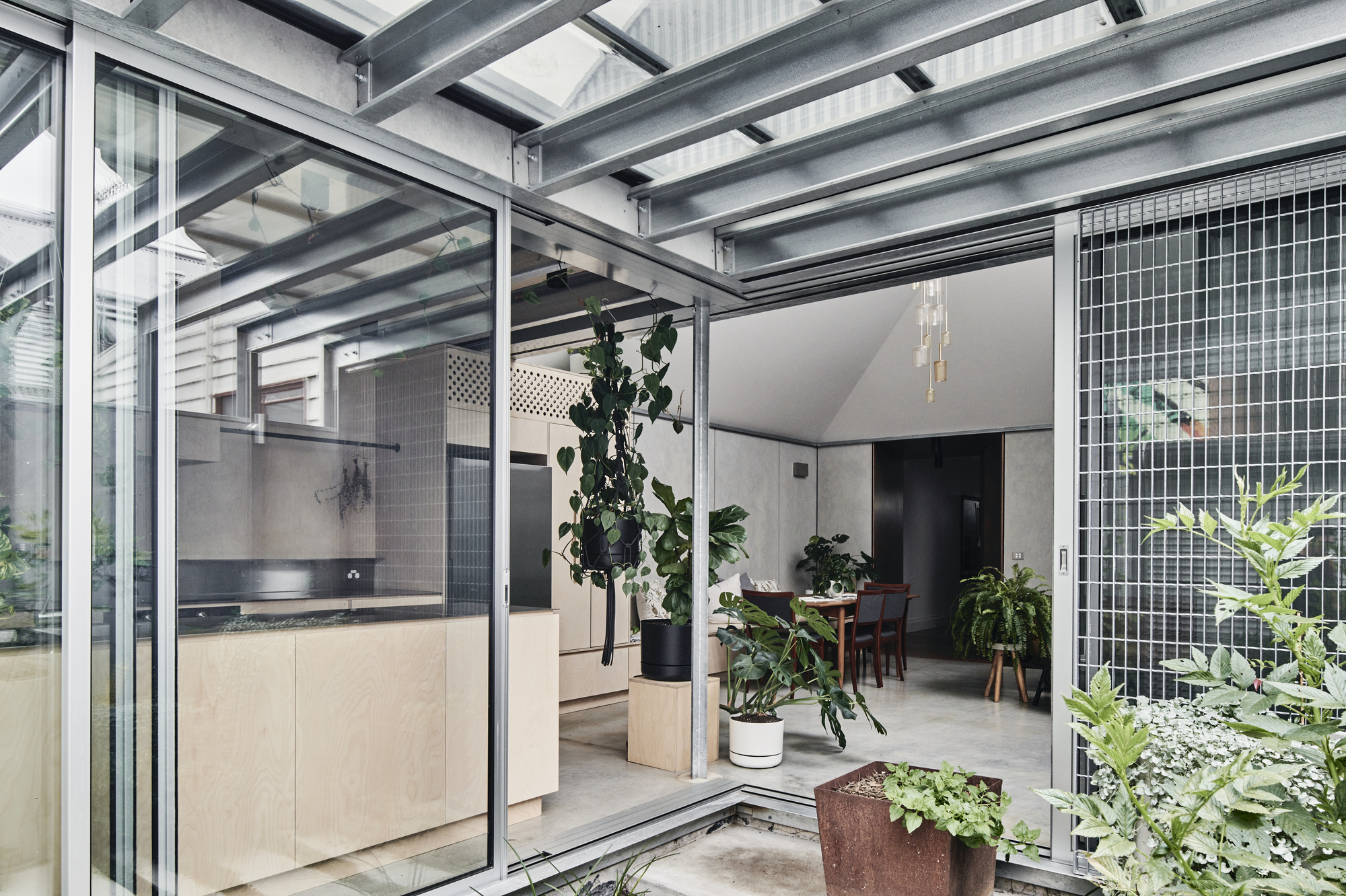 Interior looking through the glazed steel structure connecting kitchen and dining spaces with planted courtyard