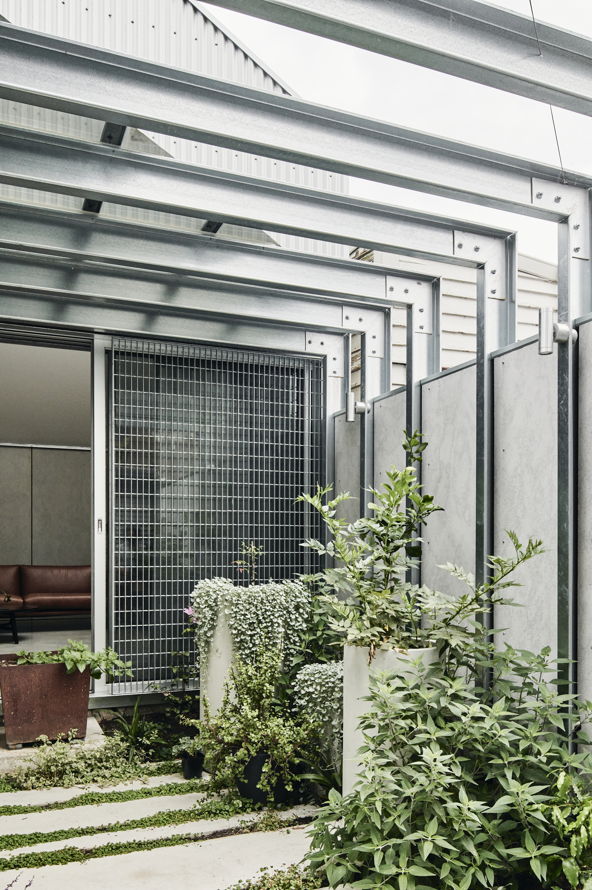Planted courtyard with grass pavers and wire mesh screen framed by steel overhead beams