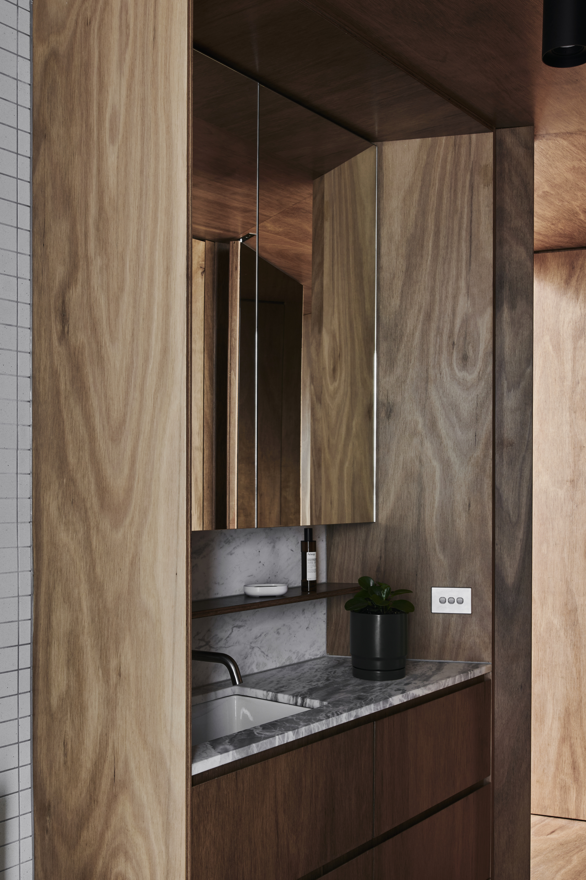 Bathroom vanity with timber cabinetry and marble countertop set within mirrored niche