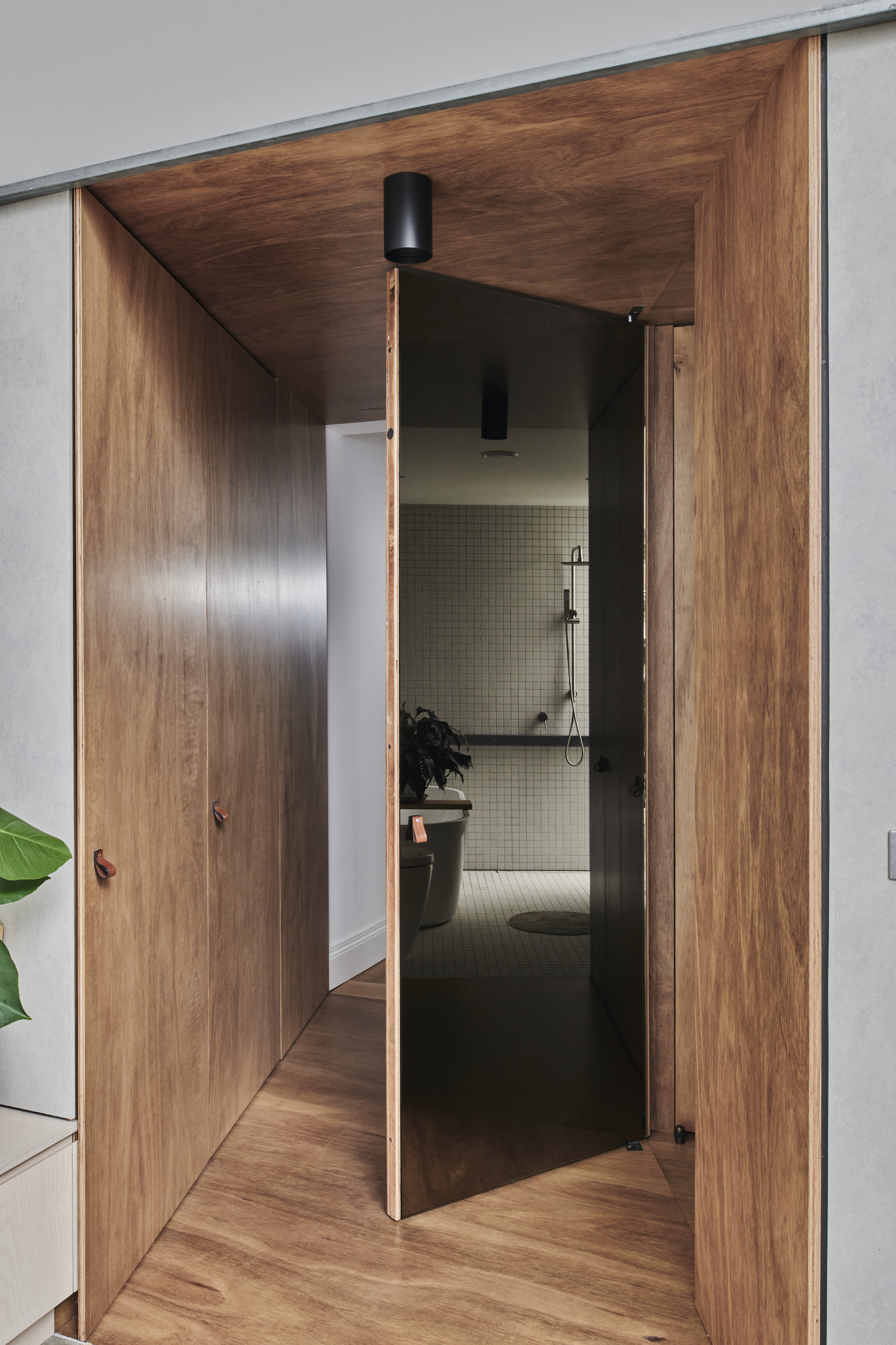 Walnut timber hallway with pivoting door revealing tiled bathroom beyond