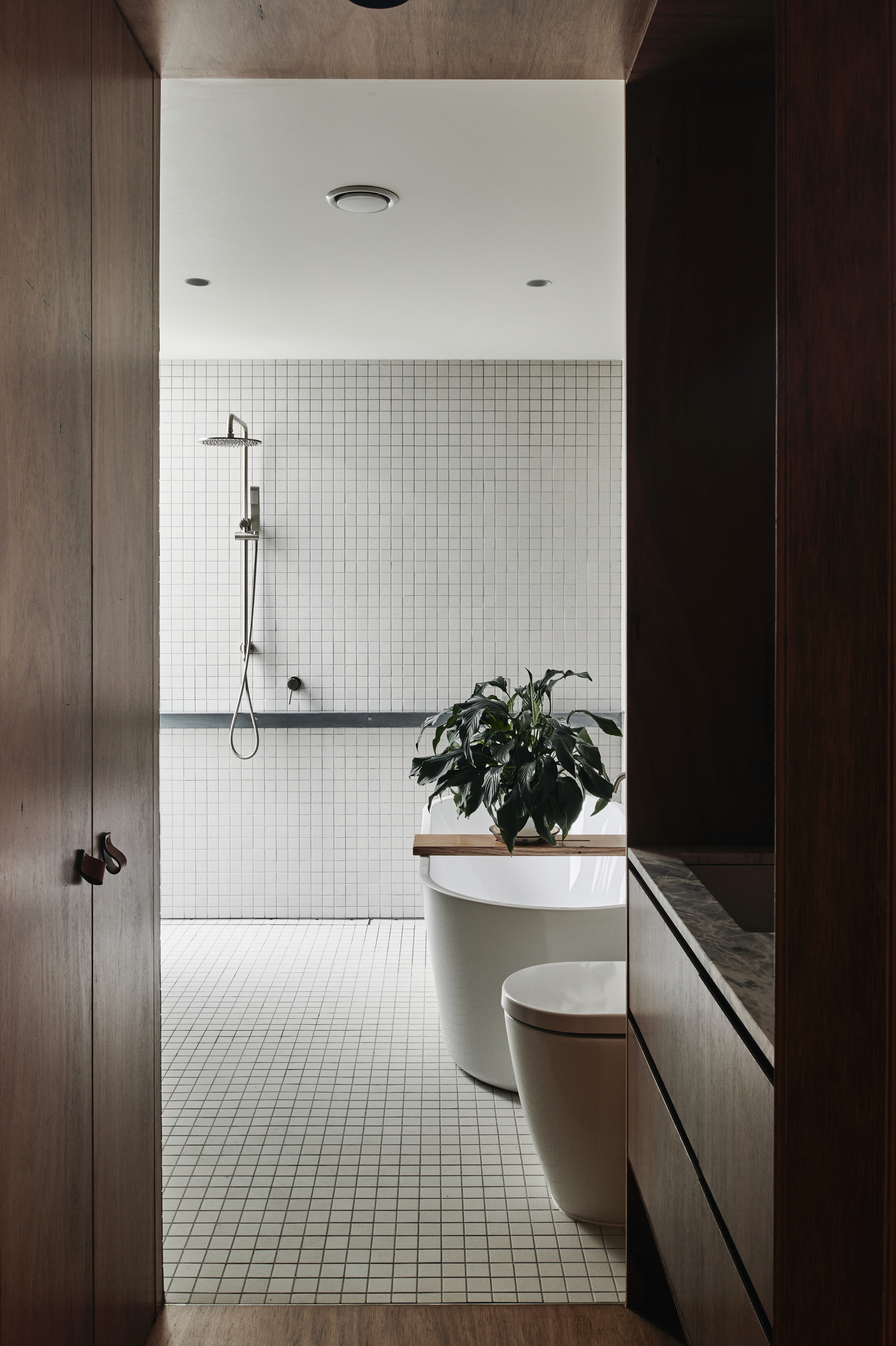 Bathroom with white mosaic tile walls, freestanding tub, and timber vanity under potted plant