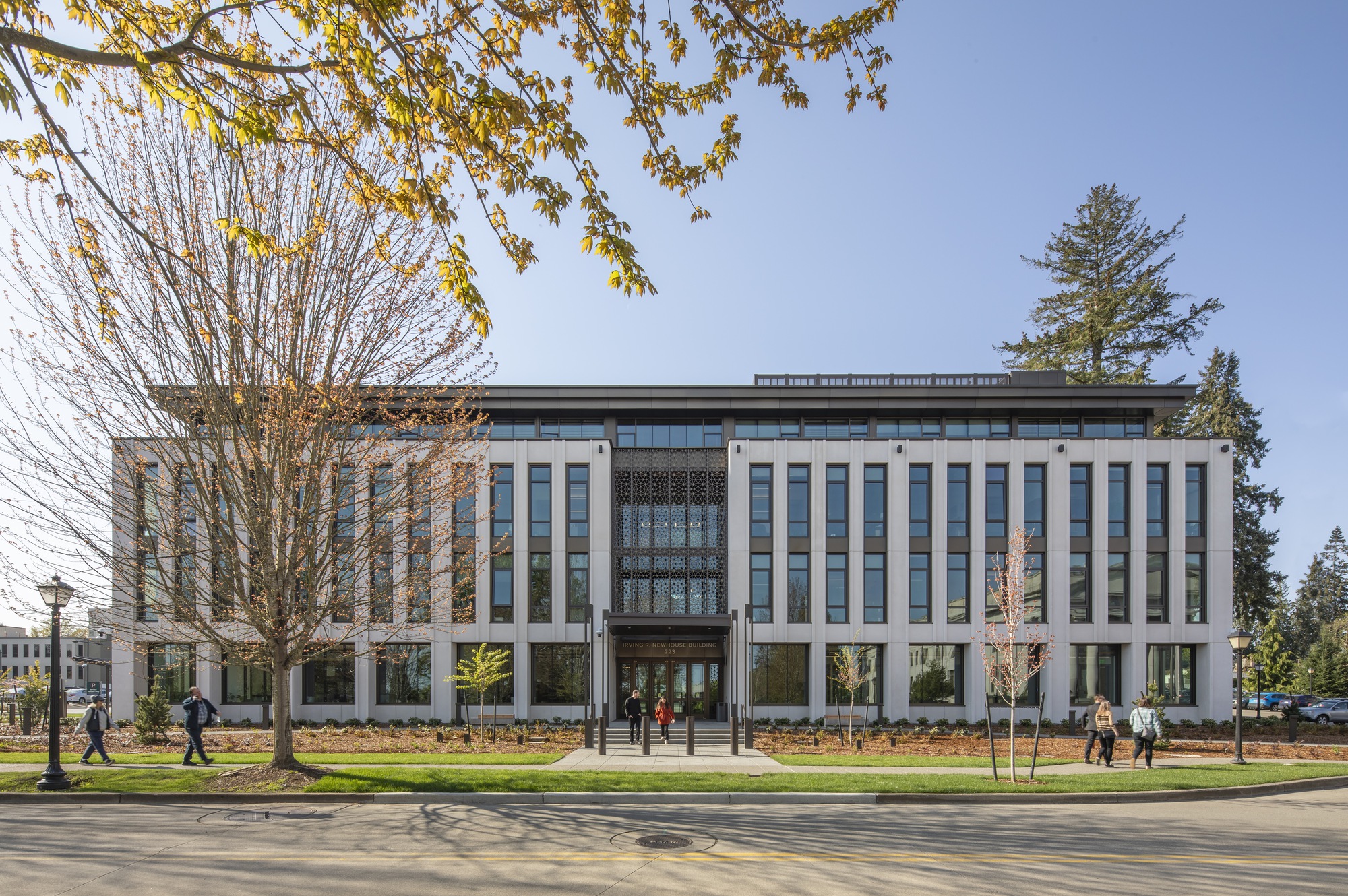 Street view of the colonnade facade with tall vertical fins framing a central patterned screen under bare spring trees