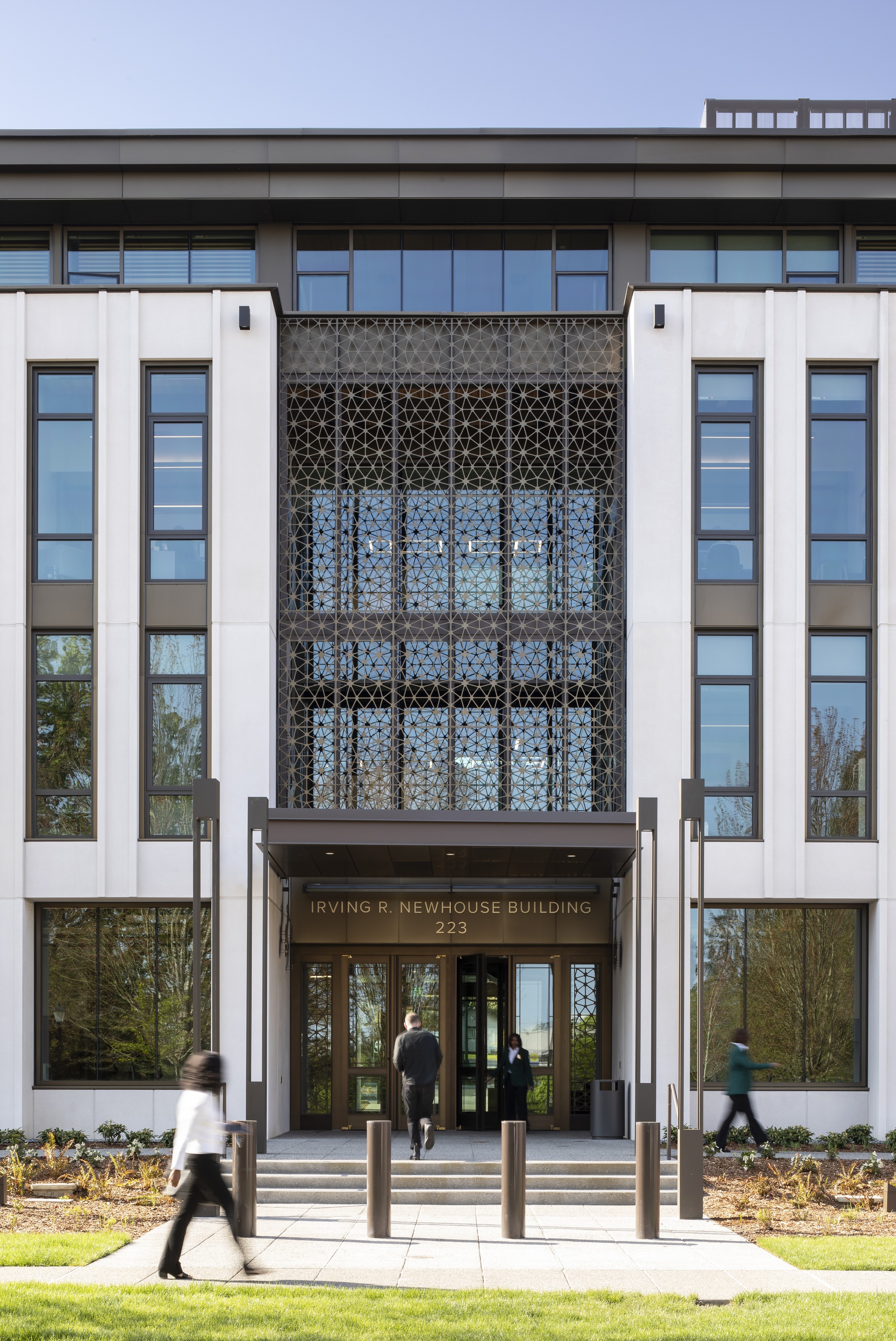 Main entrance facade with geometric patterned screen above glass doors and people walking on the pathway