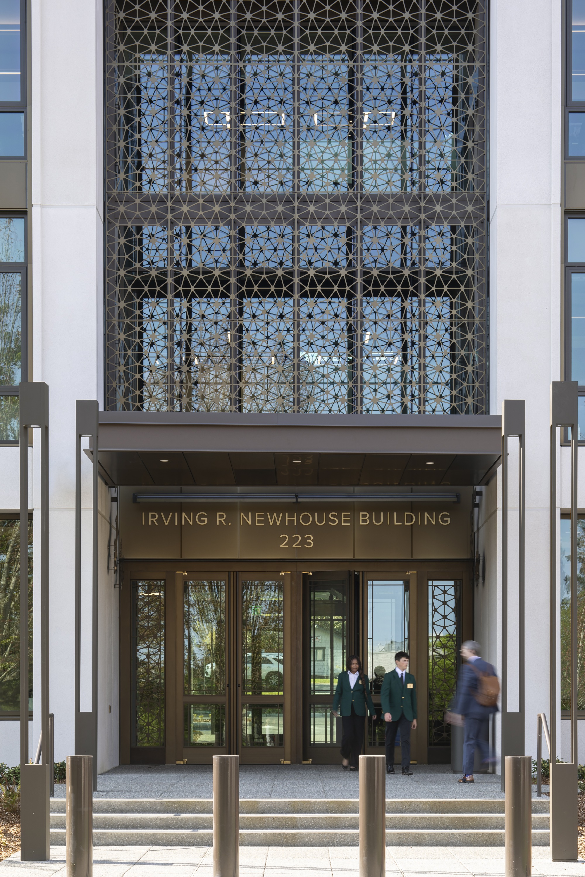 Close view of the entry canopy showing patterned metal screen with glass doors and pedestrians beneath