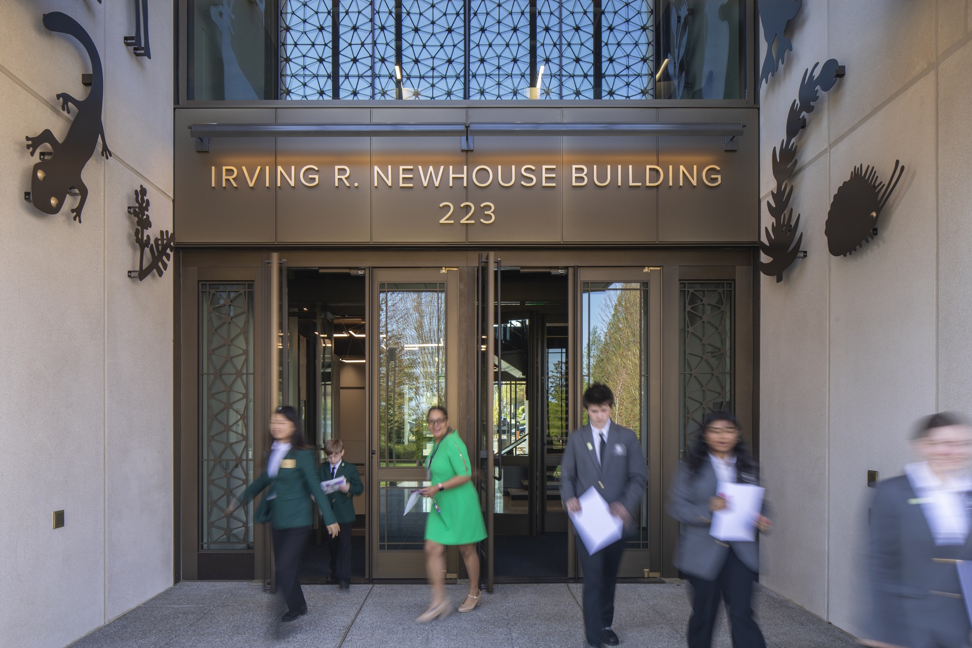 Bronze-framed glass doors with decorative metal panels and motion-blurred figures entering the lobby