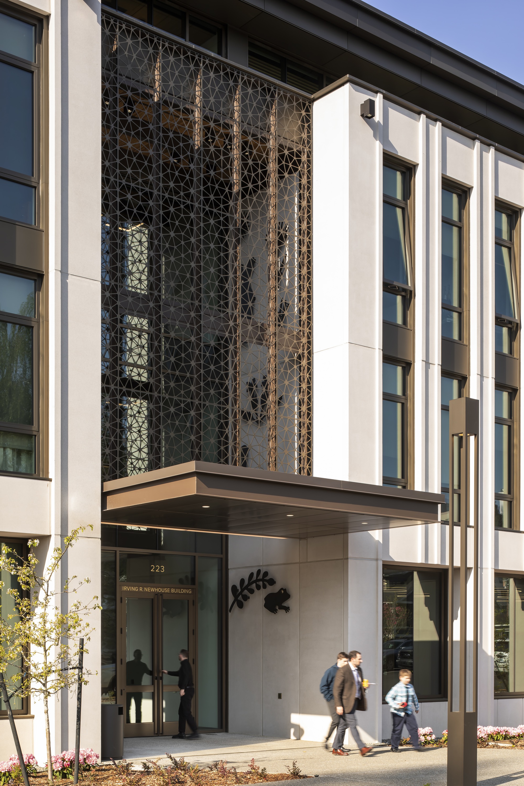 Oblique view of the entry canopy with dark patterned screen and pedestrians passing beneath in afternoon light
