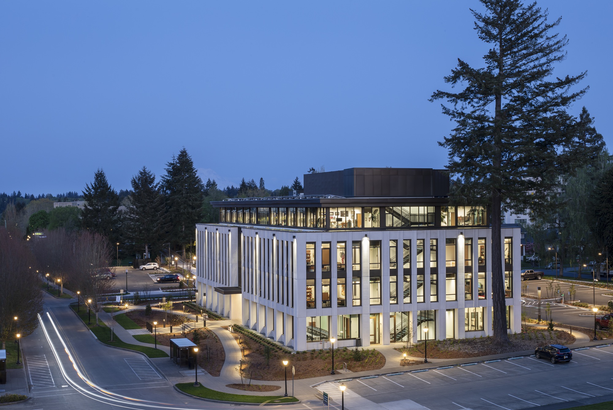 Aerial twilight view showing the corner entrance and dark rooftop volume above the illuminated glass base