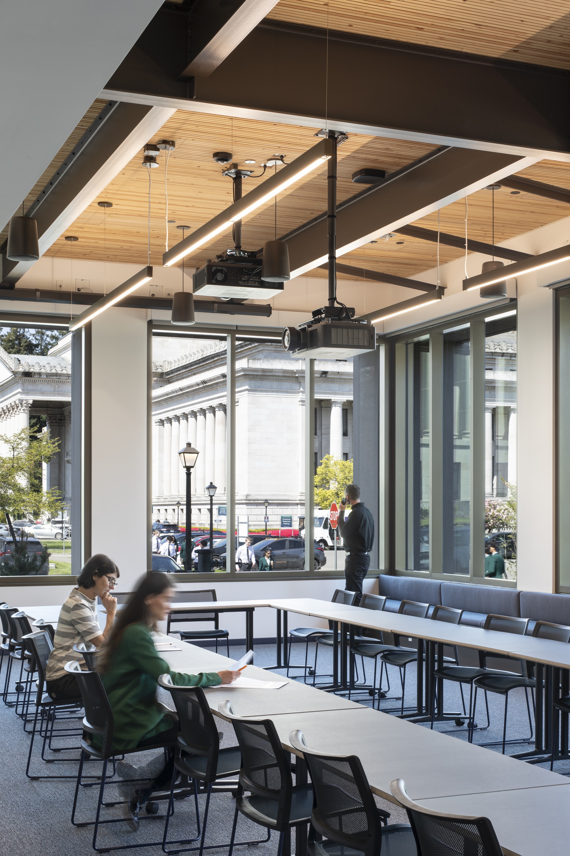 Dining area with timber-lined ceiling and floor-to-ceiling windows overlooking a street with pedestrians