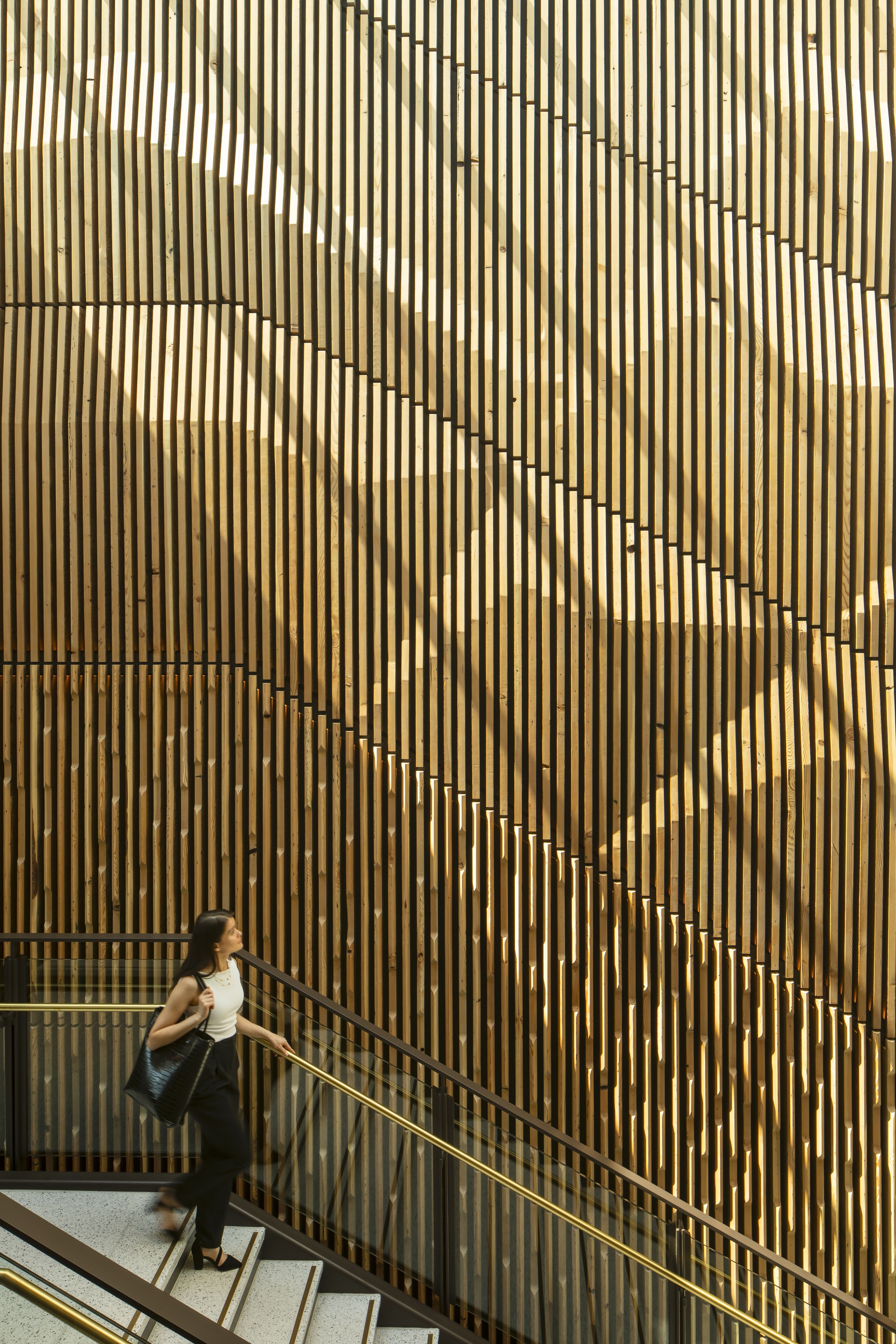 Person descending stairs alongside a patterned vertical timber screen with offset slats forming diagonal lines
