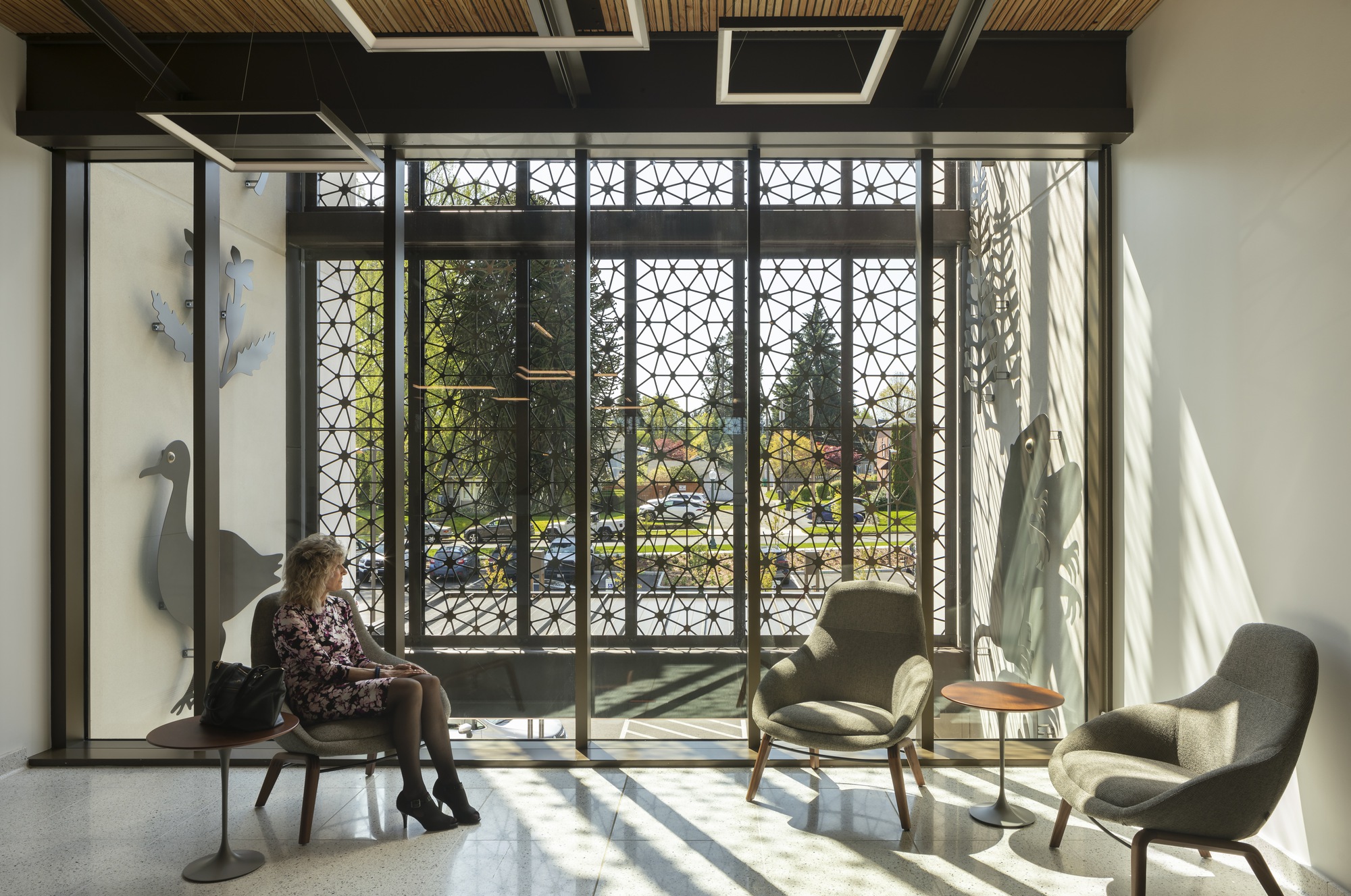 Seating area with geometric metal screens filtering sunlight and casting shadows across the floor