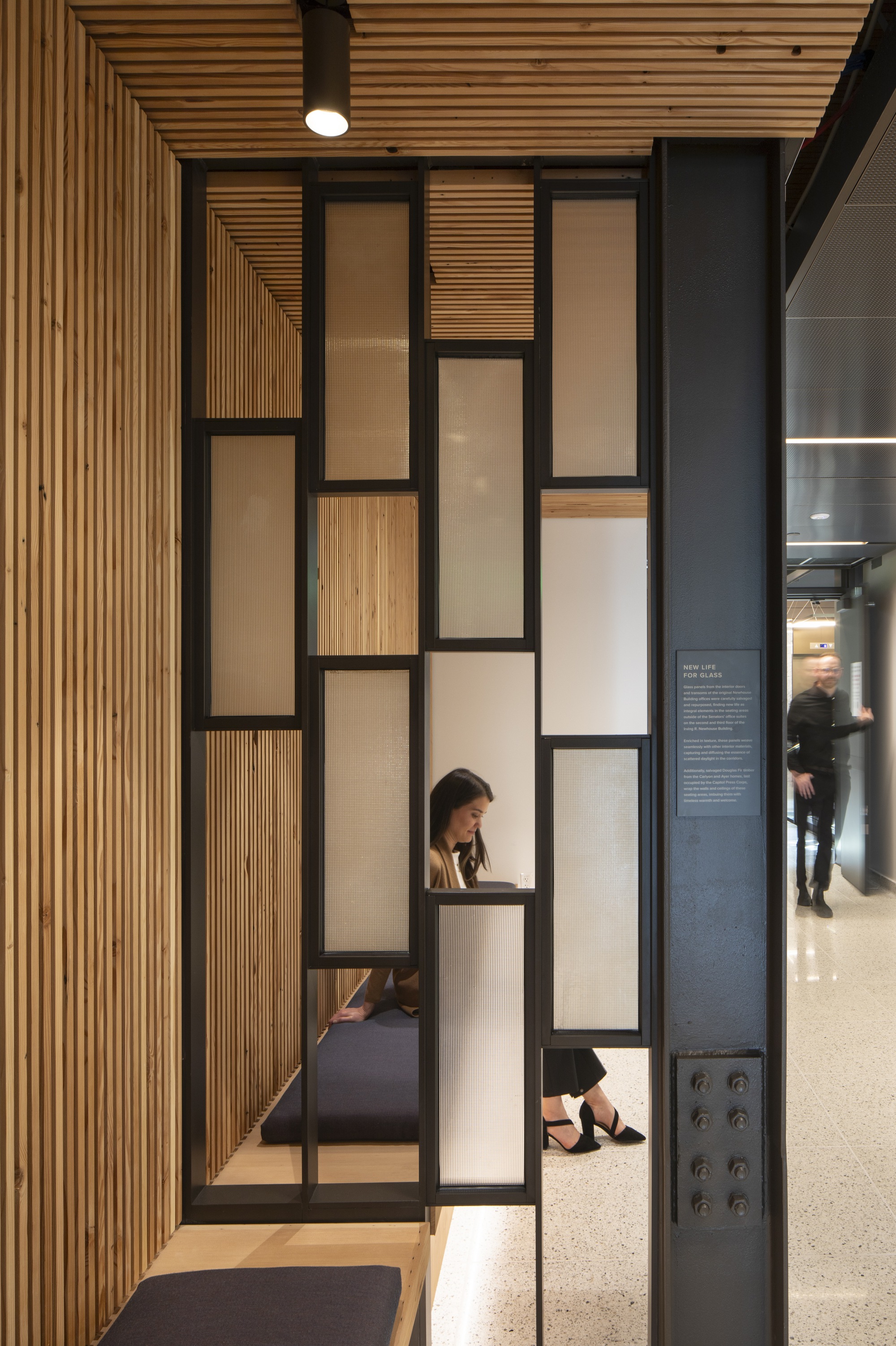 Black steel frame partition with alternating timber and frosted glass panels beside timber slat wall