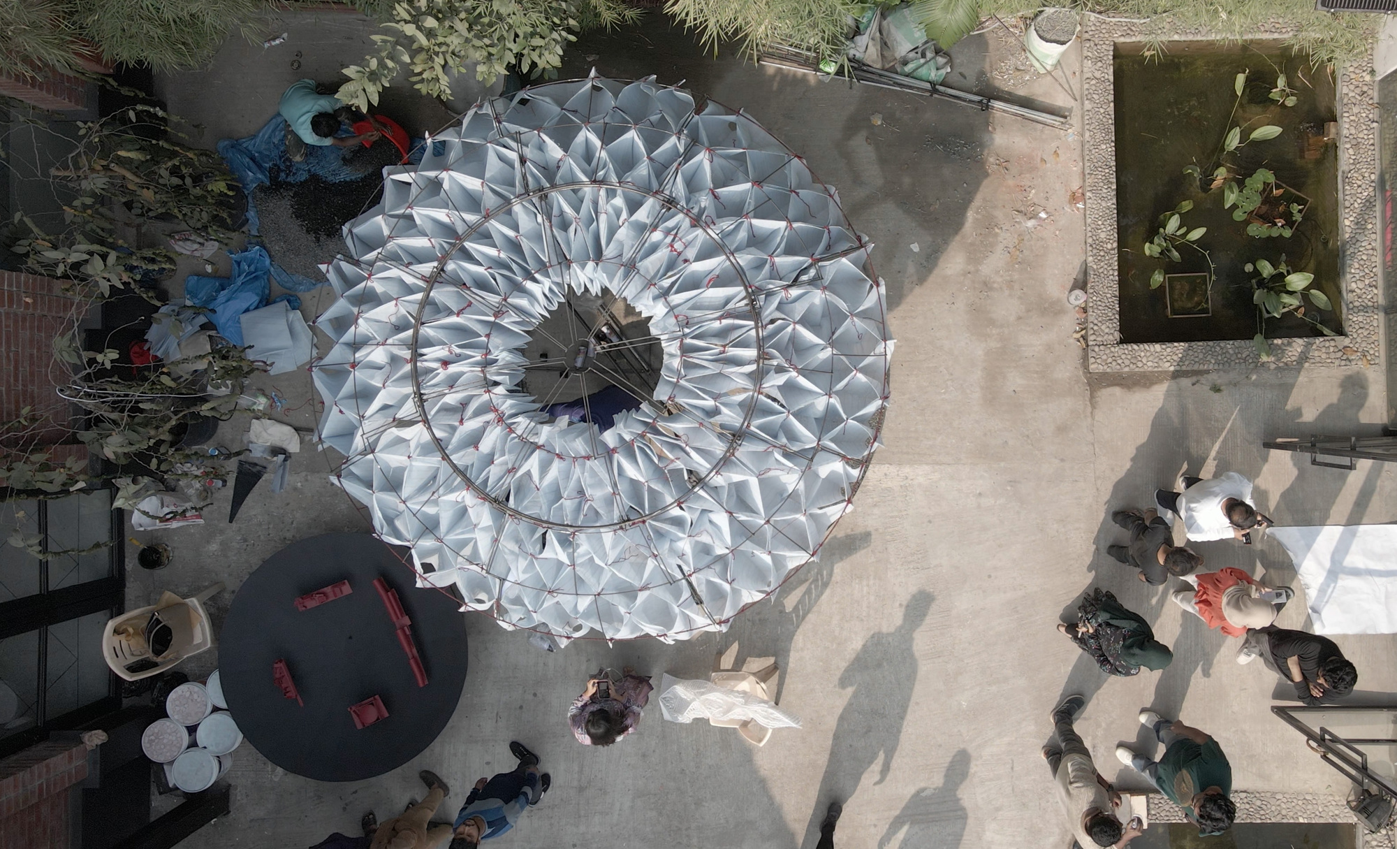 Aerial view of the radial folded fabric canopy with visitors gathering on the concrete plaza