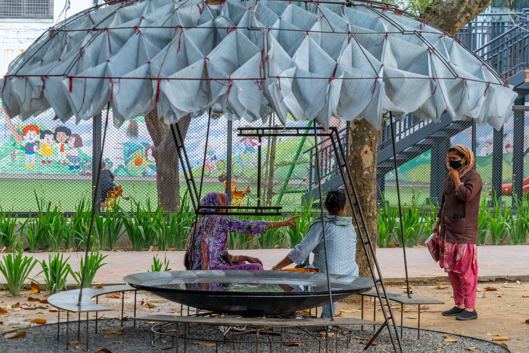 Circular pavilion with pleated fabric canopy and steel frame sheltering children on a raised platform