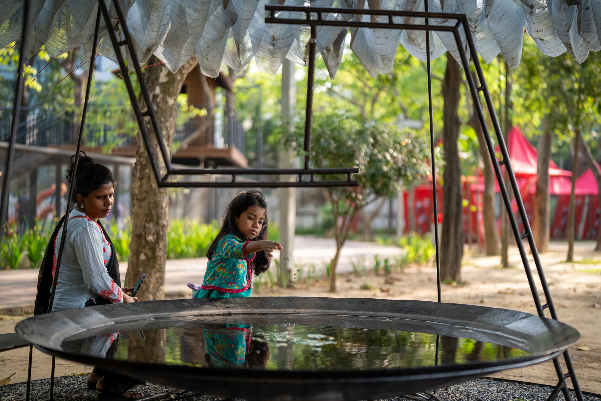 Two figures beside the circular water basin under the steel frame and fabric canopy