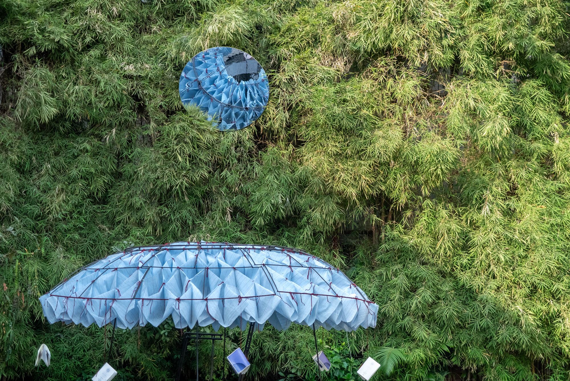 Aerial view of two pavilions with pleated canopies set against a dense bamboo hillside