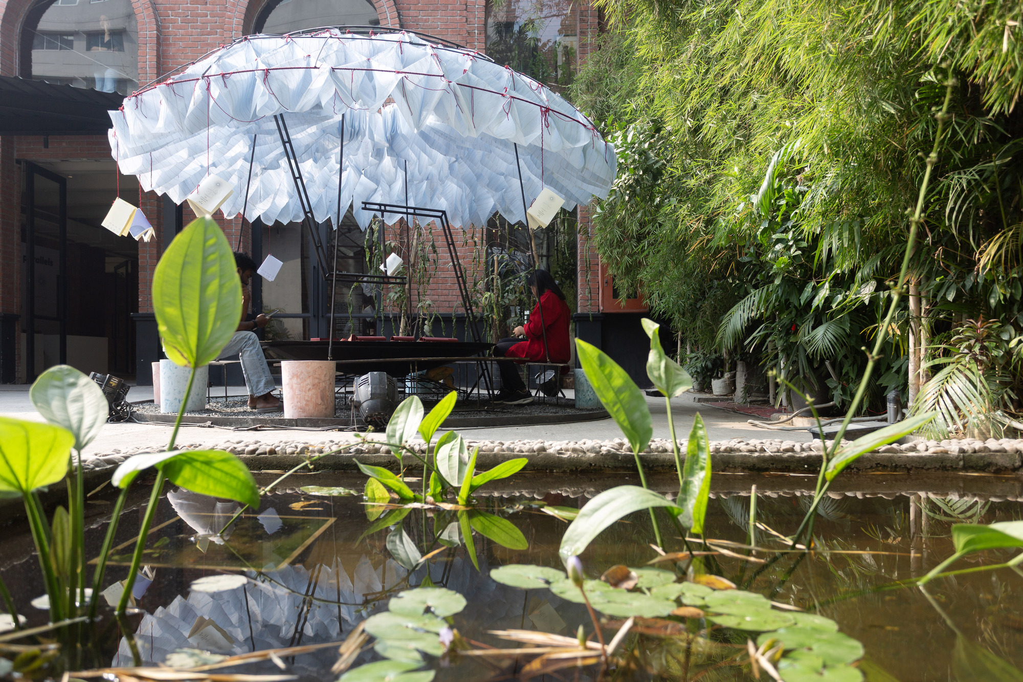 Canopy pavilion viewed across a pond with lily pads and aquatic plants in the foreground
