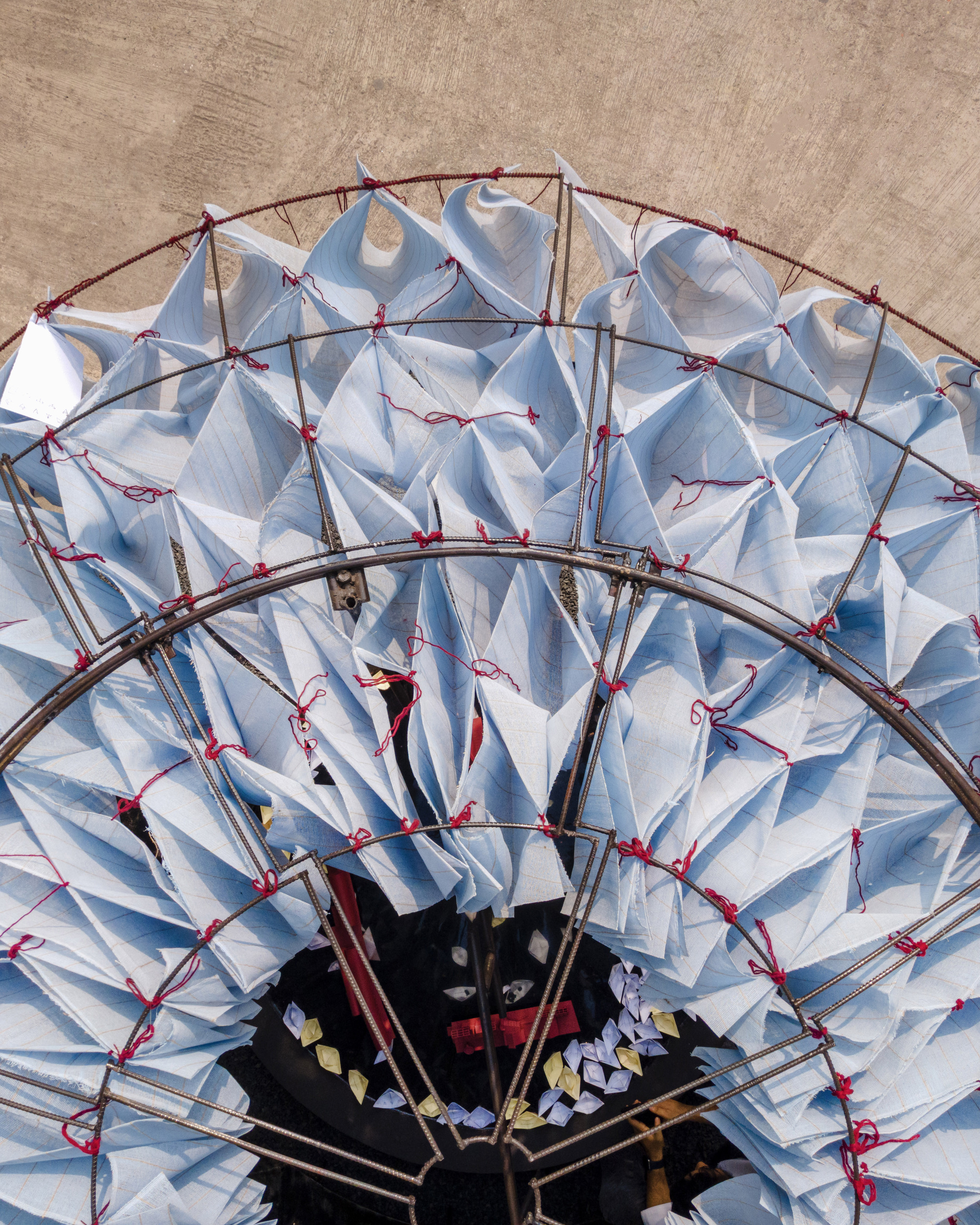 Overhead view of pleated white fabric canopy stretched over a curved metal frame with red cord ties