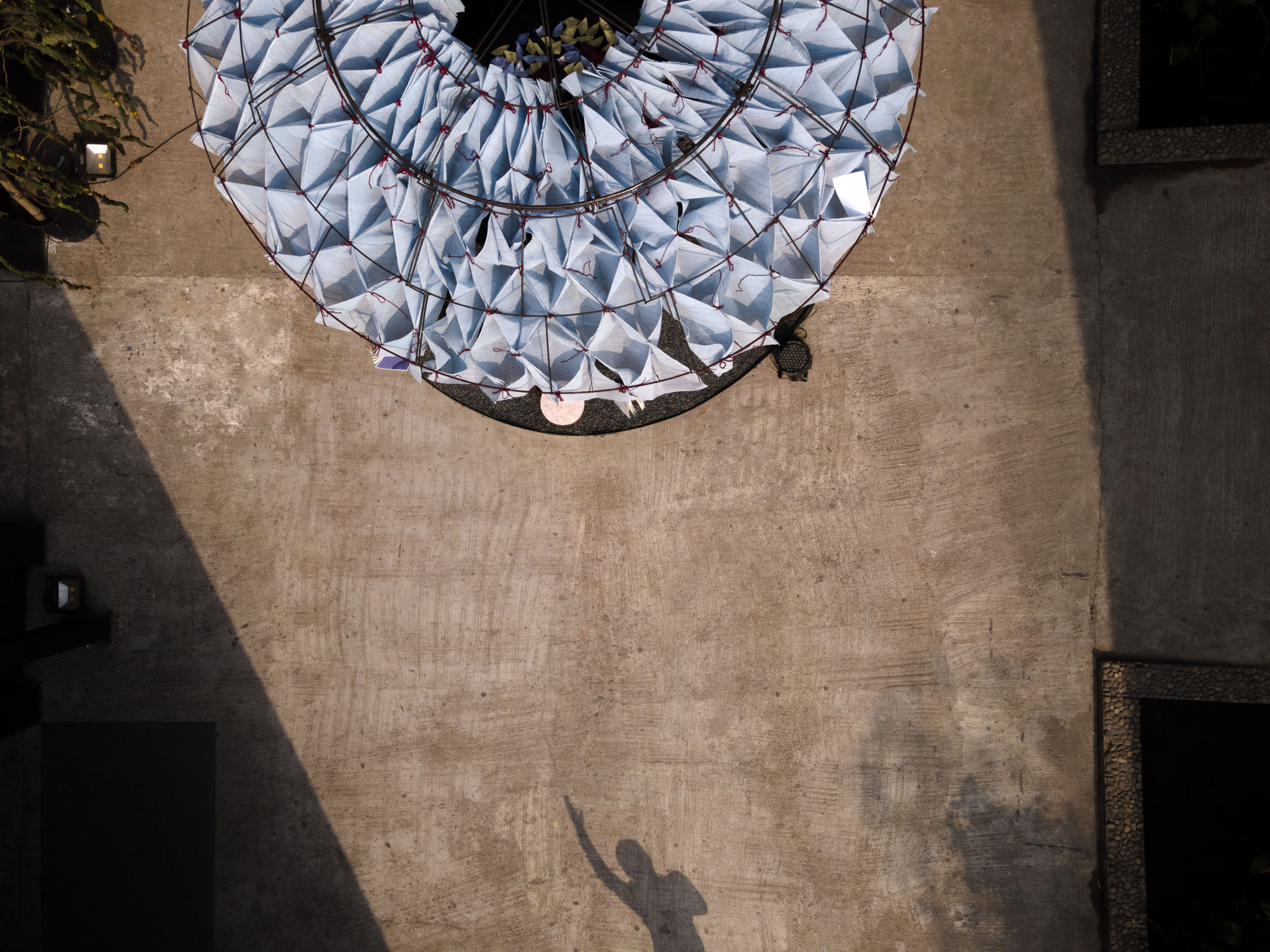 Aerial view of circular fabric canopy casting shadows on concrete paving below in afternoon sunlight