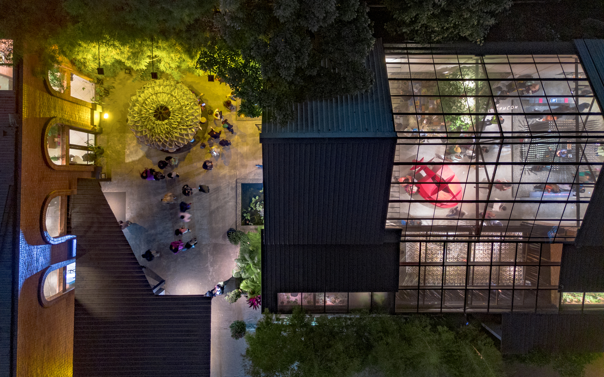 Aerial view at night of courtyard with circular skylight and glazed facade with people gathered below