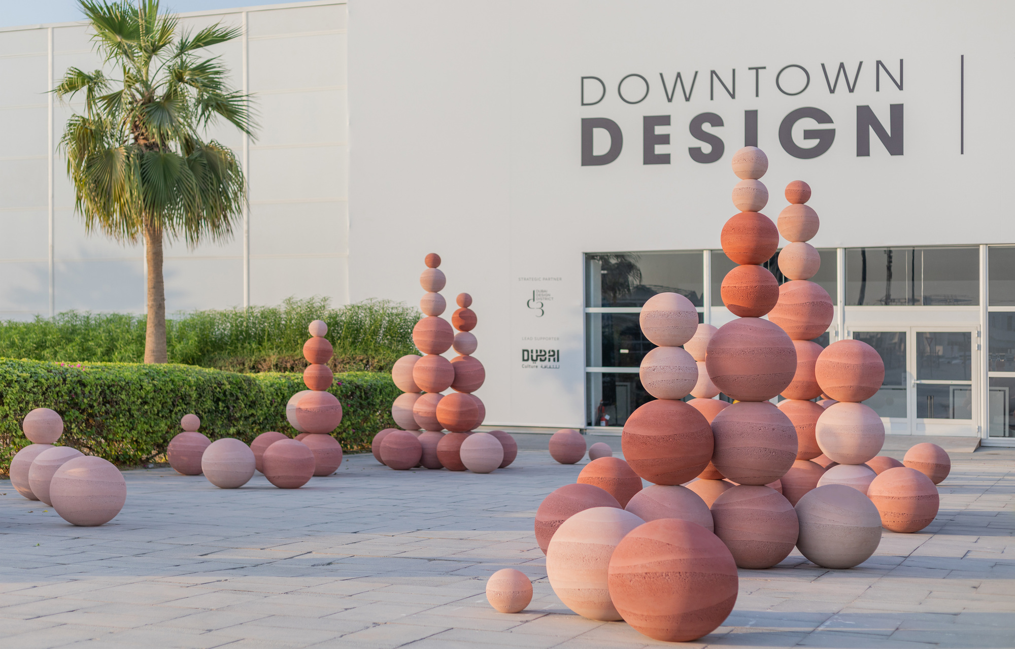 Grouped ceramic sphere sculptures arranged before a glazed entrance and trimmed hedge