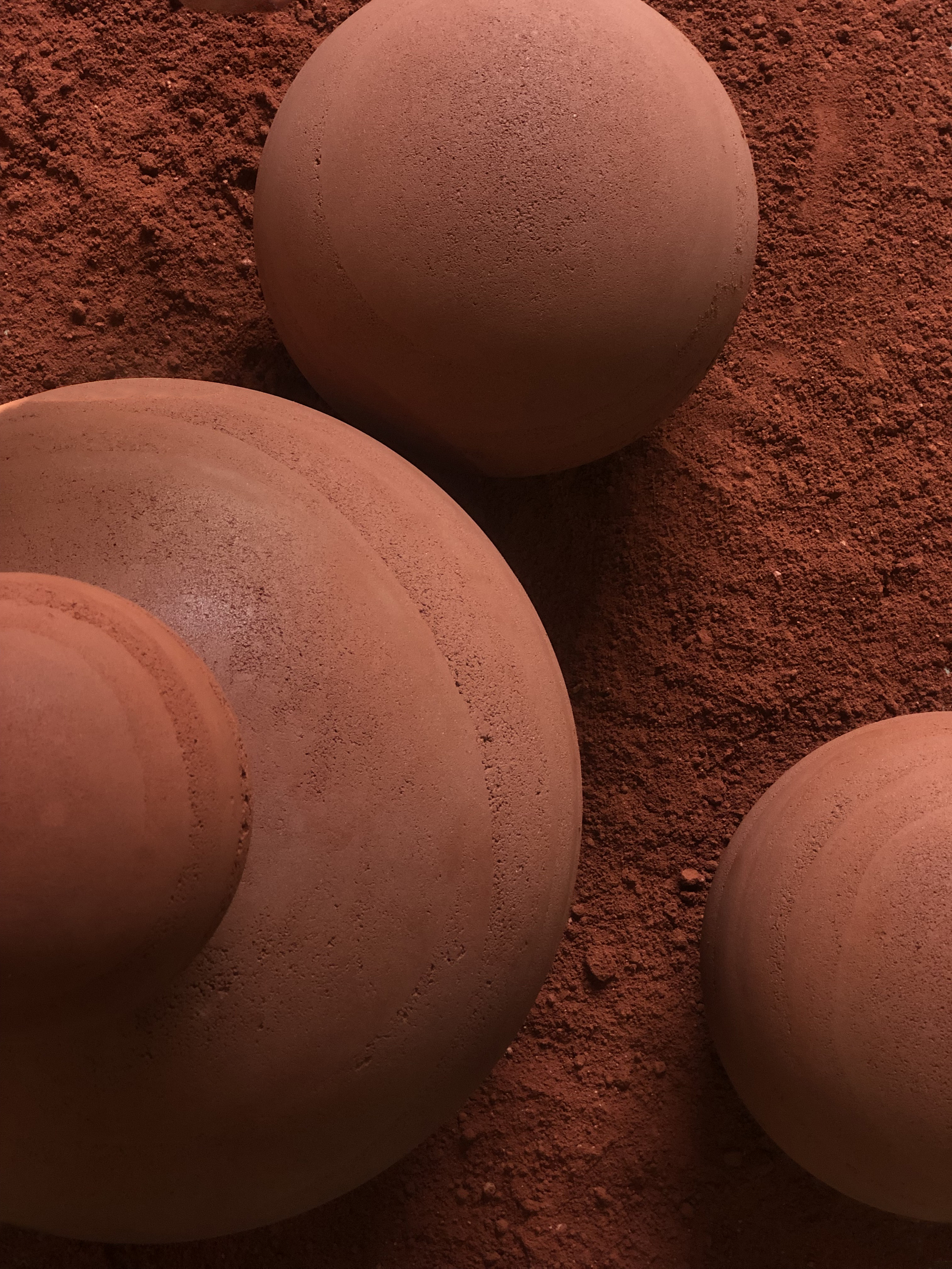 Close-up of textured terracotta spheres meeting red soil showing surface seams and grain