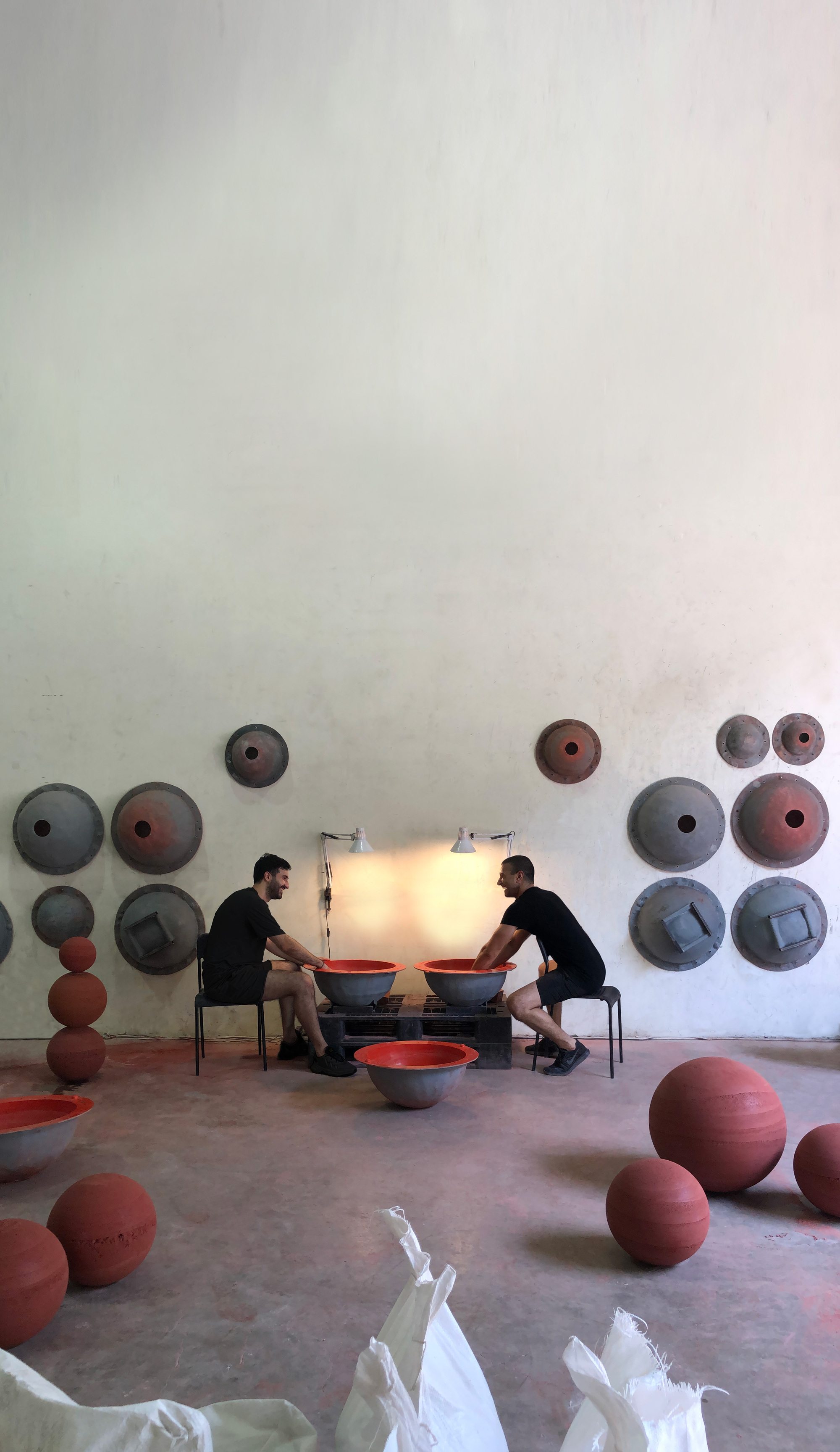 Interior studio with two people working at a table surrounded by ceramic discs and spheres