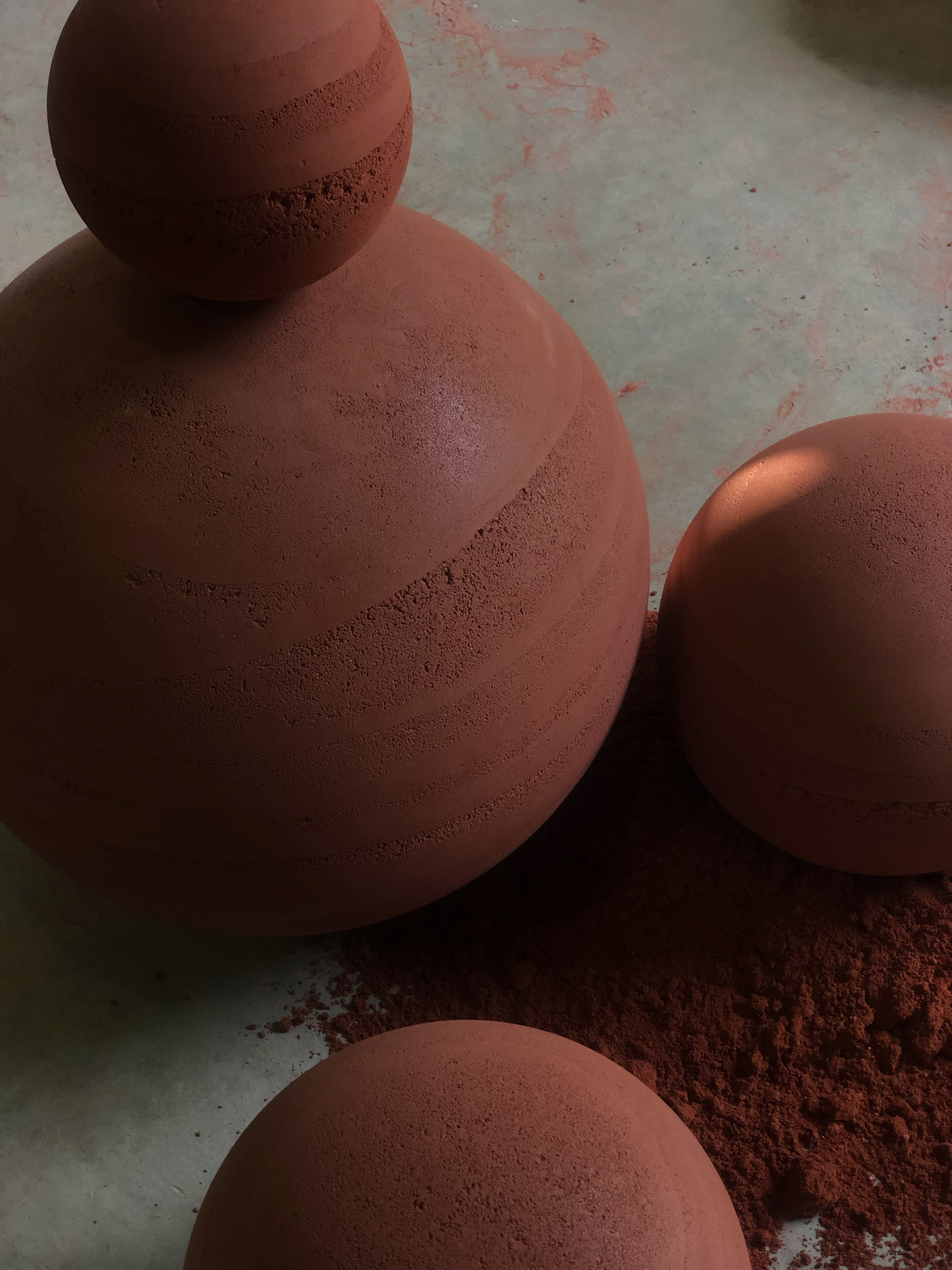 Stacked terracotta spheres casting shadows on pale concrete flooring with pigment dust