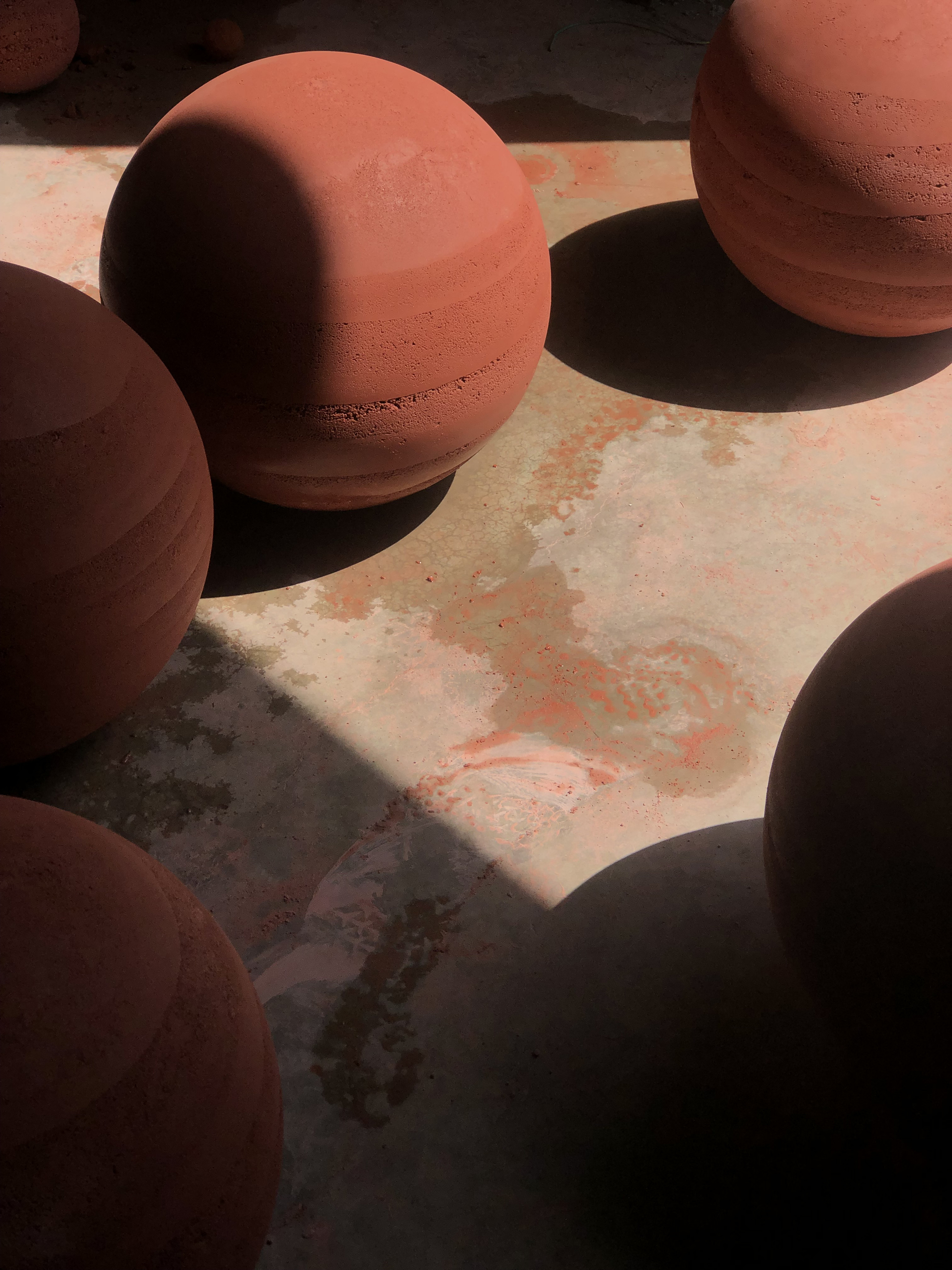 Terracotta sphere on concrete paving with sharp shadows in bright sunlight