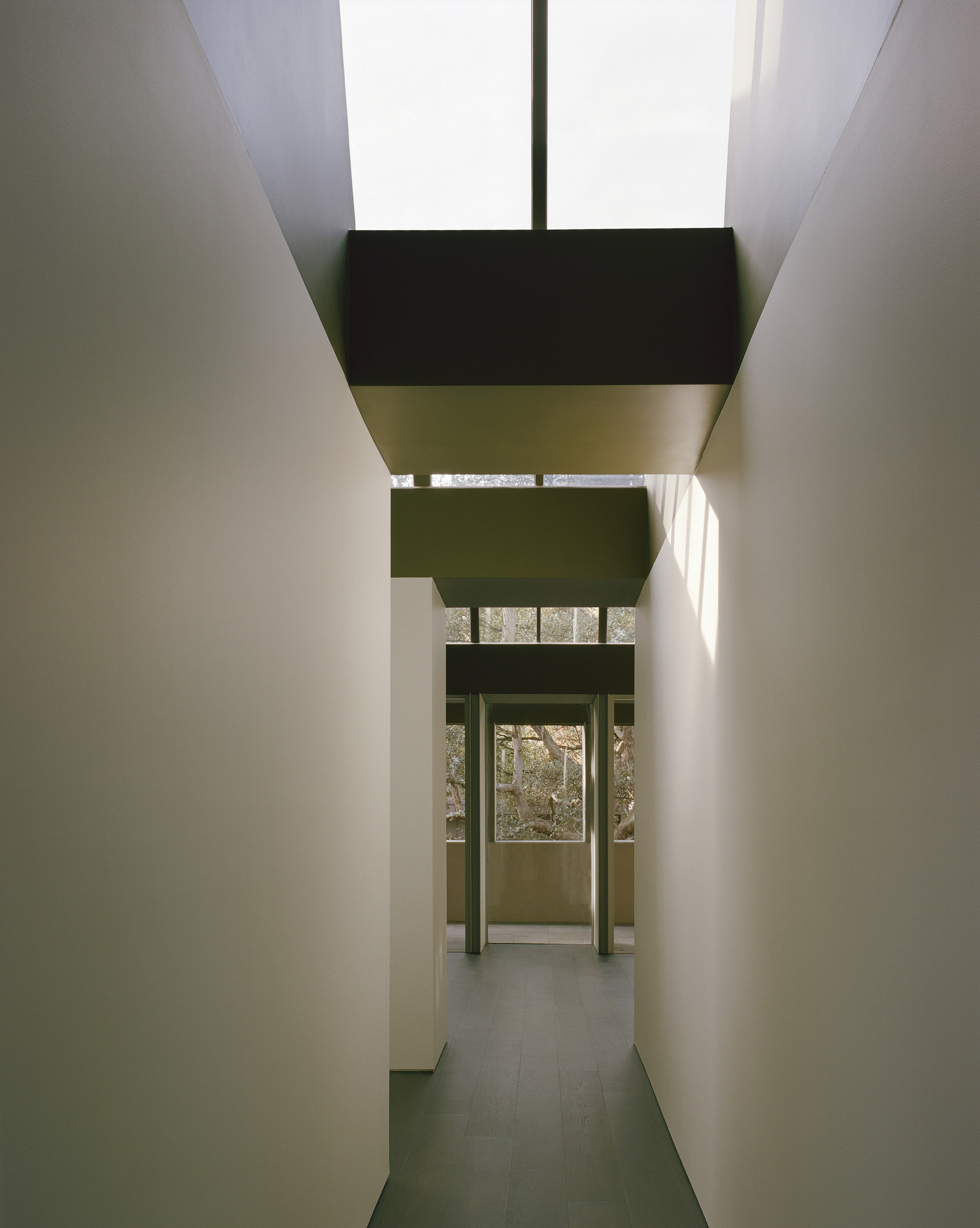 Narrow corridor with stacked clerestory volumes casting daylight onto pale plaster walls