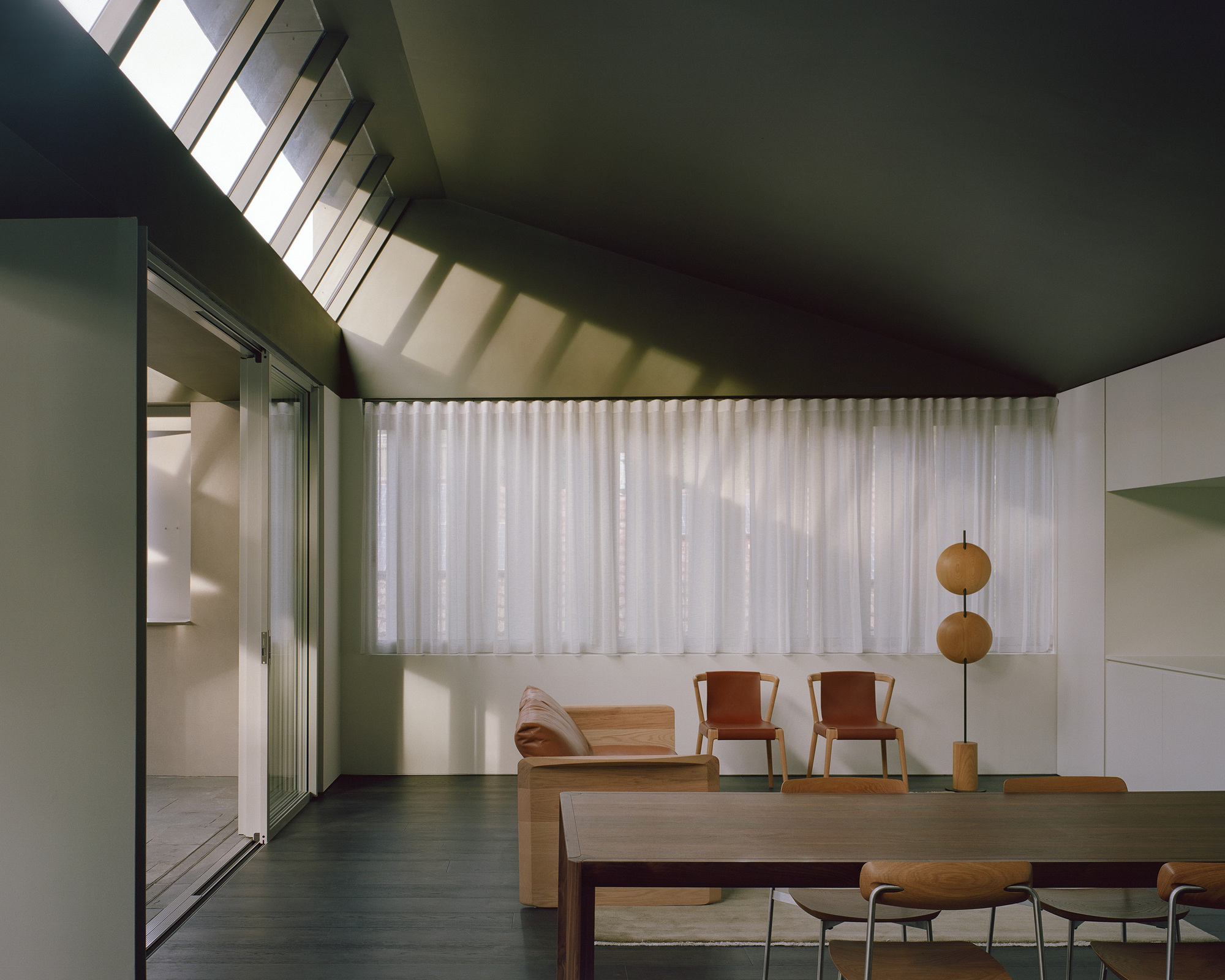 Living area with clerestory windows casting shadows across sheer curtains and timber furniture
