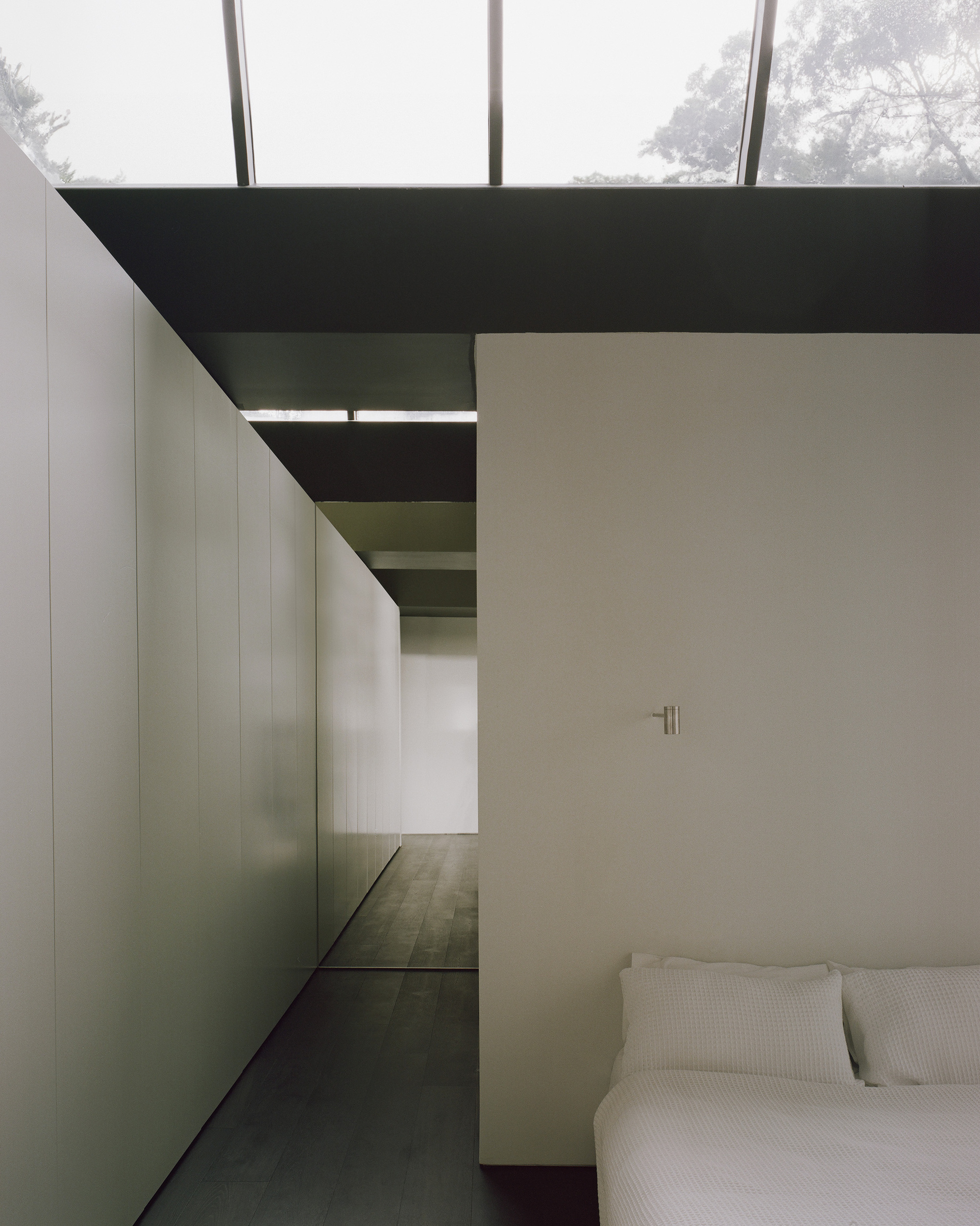 Bedroom with dark timber flooring and glimpse of adjoining spaces through tall steel-framed glazing