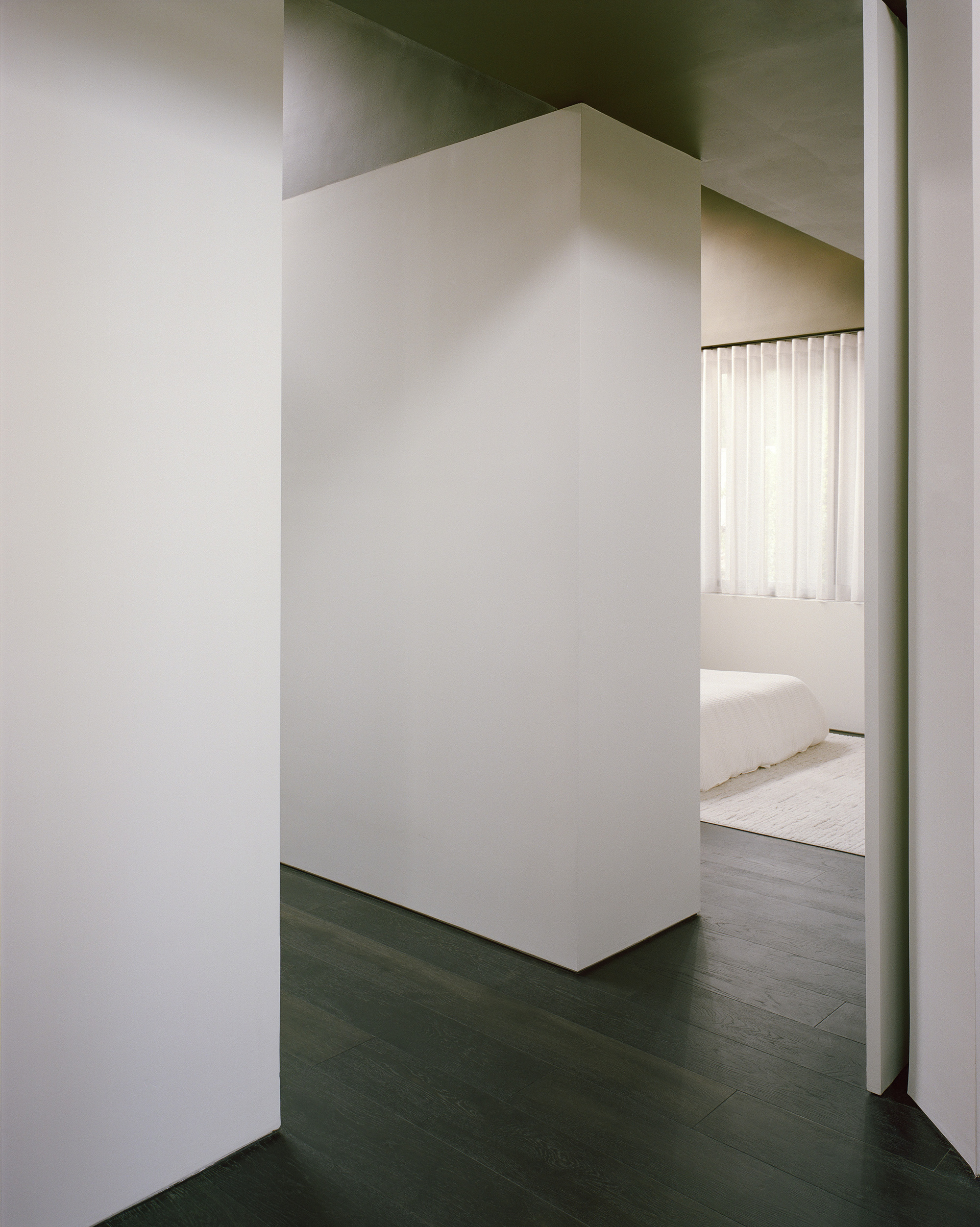 Freestanding plaster volume dividing circulation space from bedroom with vertical blinds
