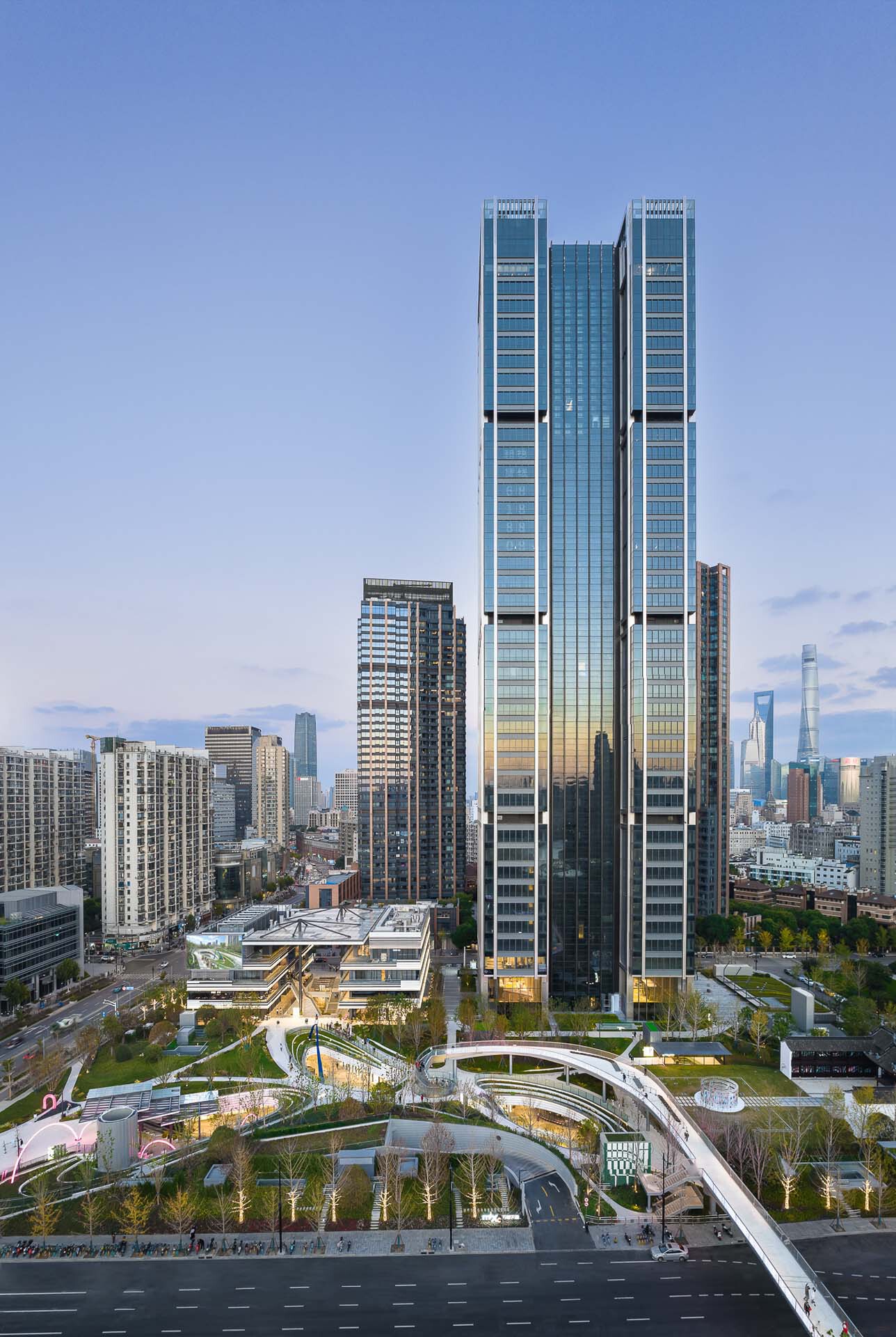 Twin glass towers rising above a layered podium with planted terraces at dusk
