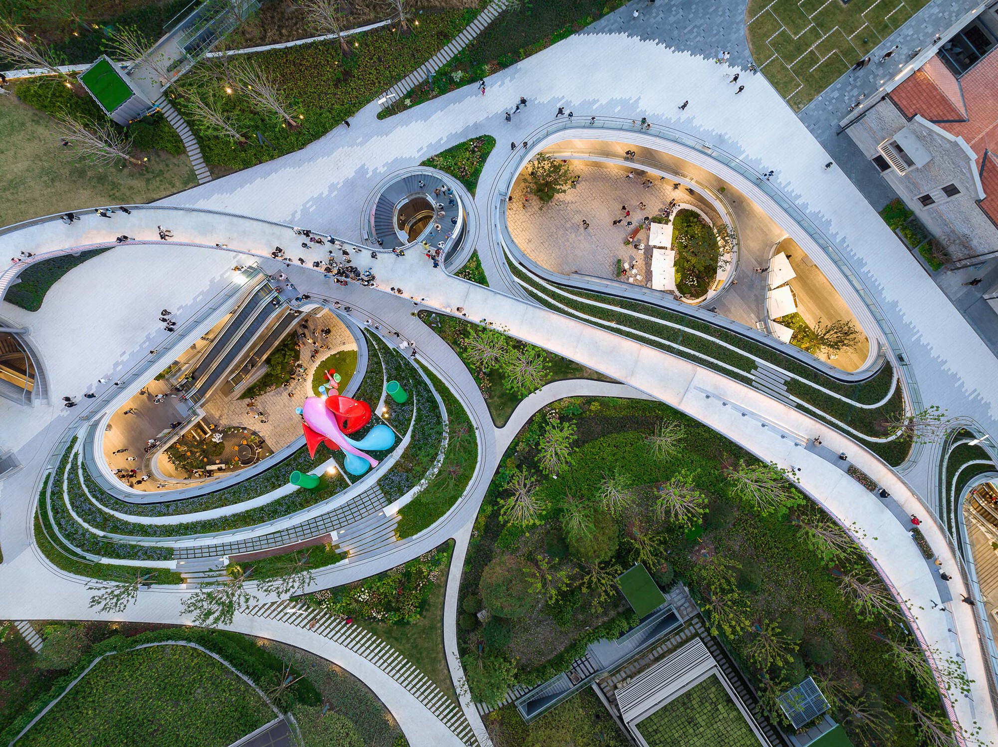 Overhead view of looping terraced walkways surrounding sunken courtyards with sculptural play elements