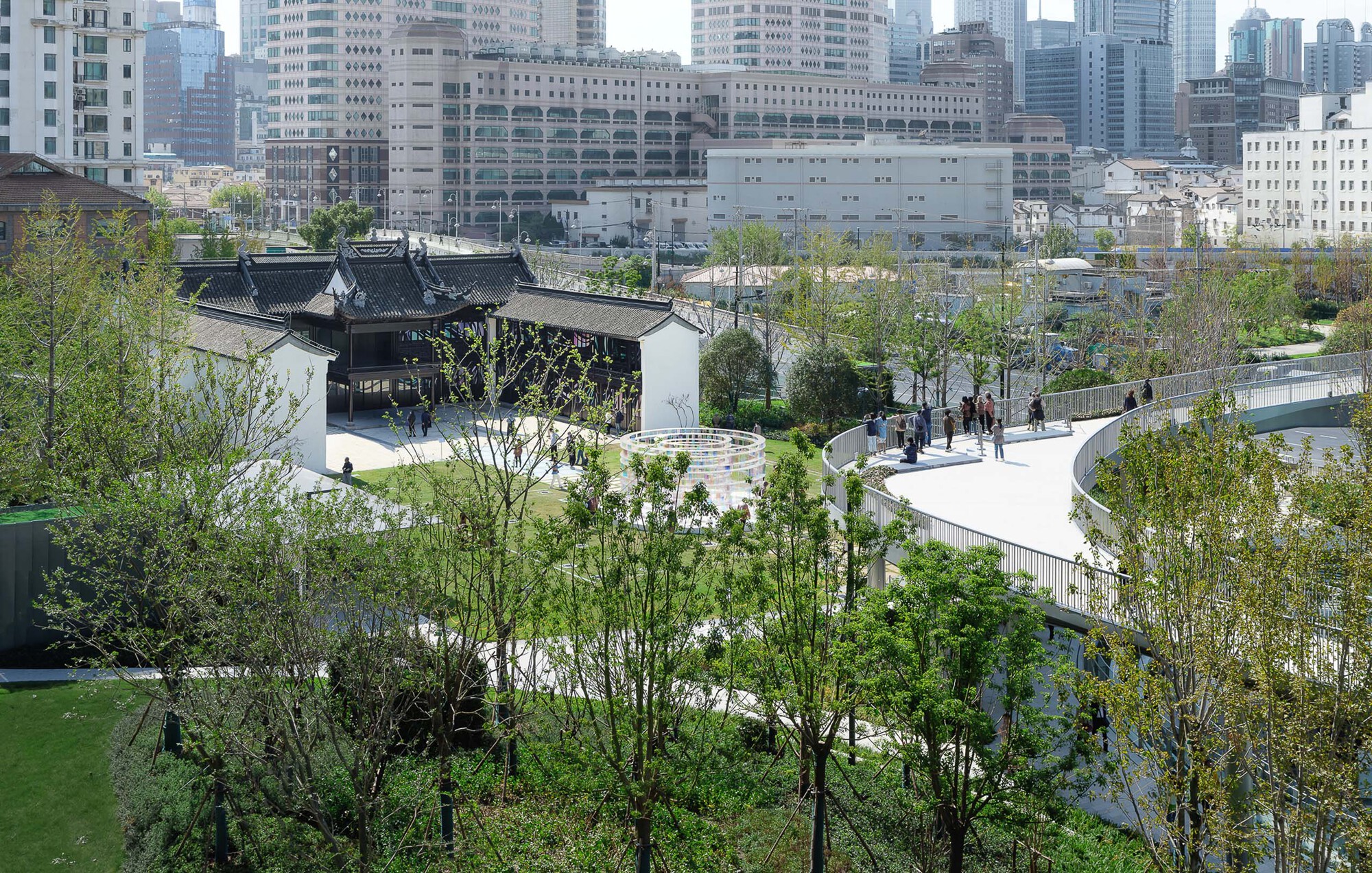 Elevated view of traditional pavilion with black-tiled roof set within terraced landscape and young trees