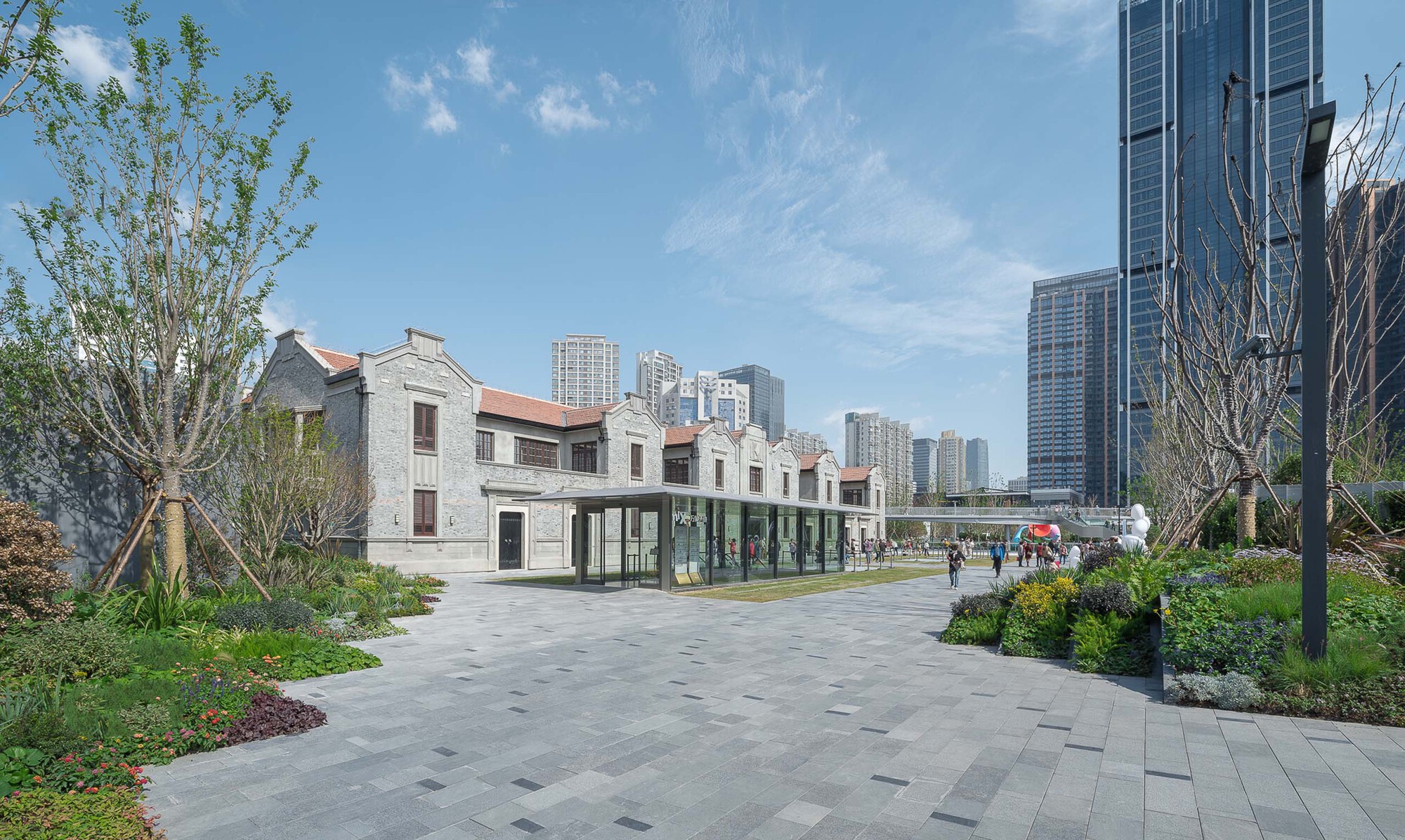 Paved plaza with restored grey brick houses and glass-enclosed link building framed by young trees