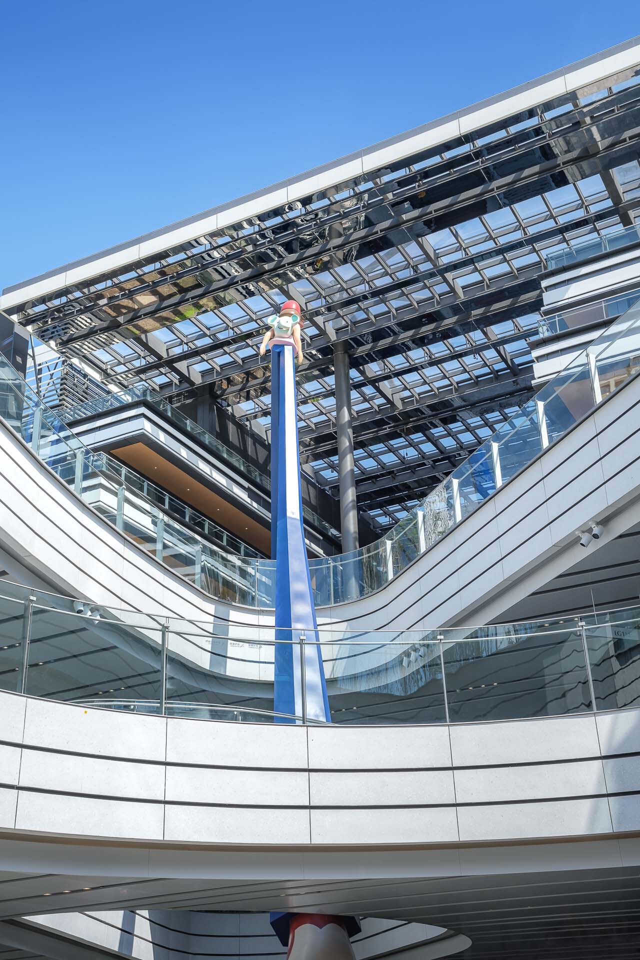 Interior atrium looking up at the curved solar panel canopy and blue column against clear sky