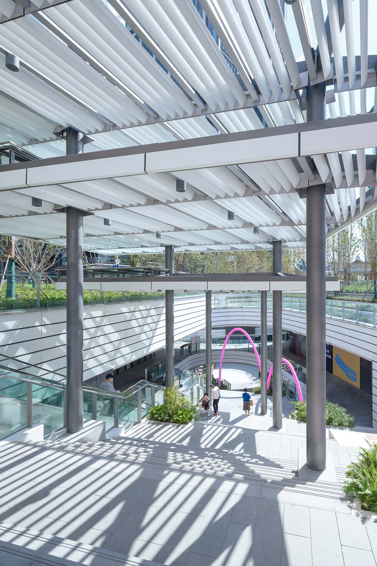 Upper terrace with horizontal cable railings and white louver canopy casting striped shadows in bright sunlight