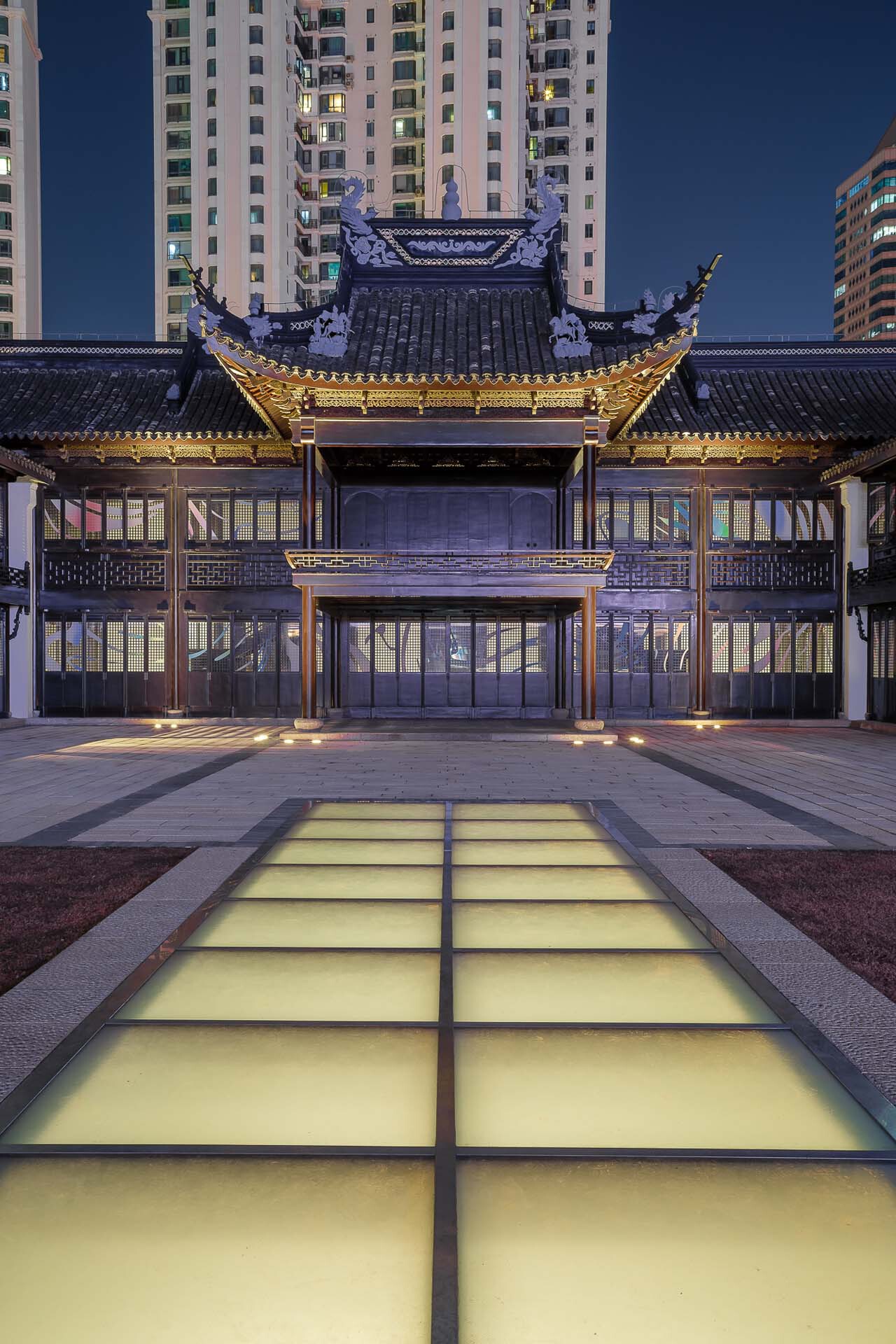 Illuminated floor skylights stretching toward the layered timber roof structure at dusk