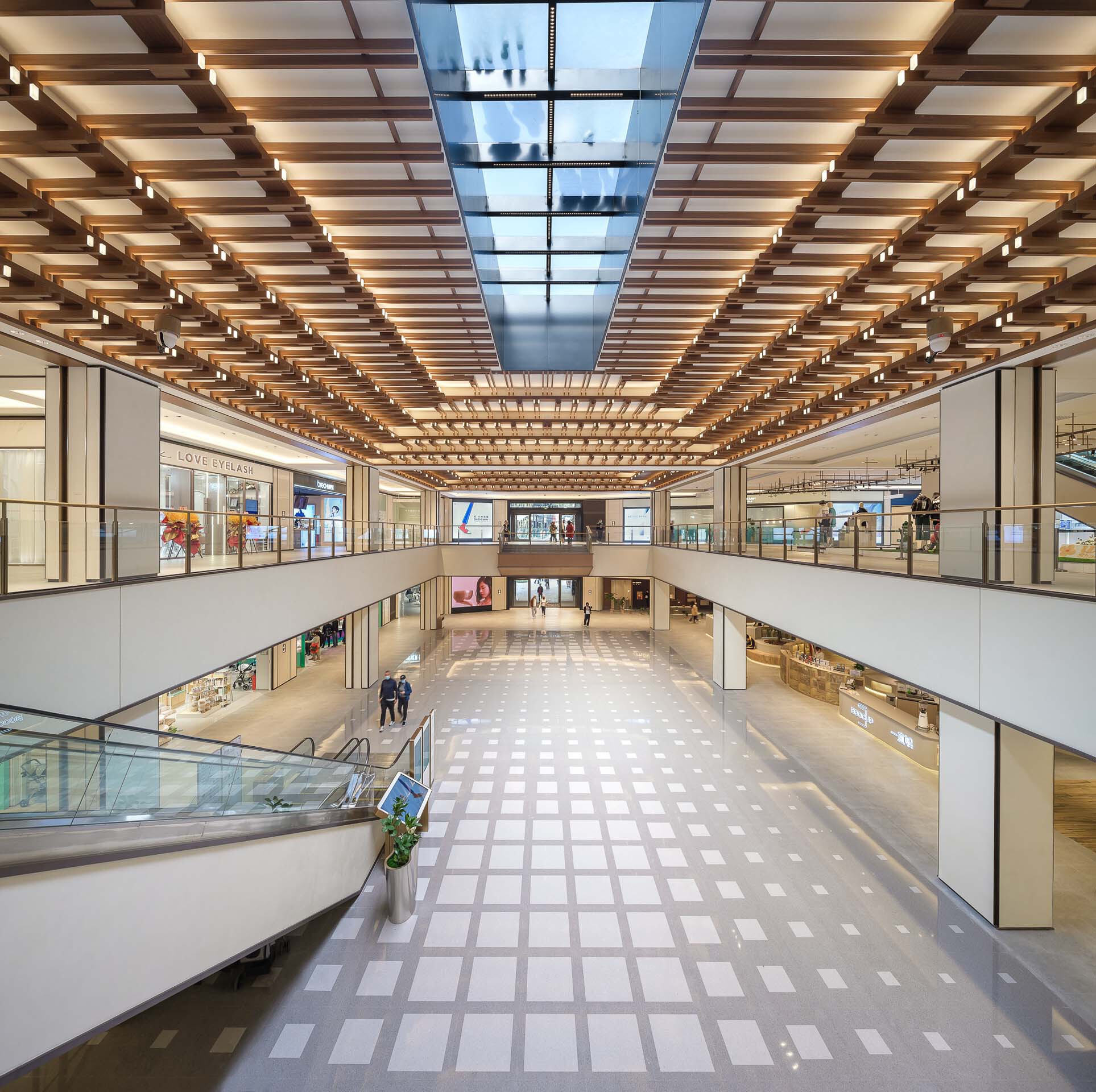 Multi-level atrium with gridded skylight and timber slat ceiling above balconies and storefronts