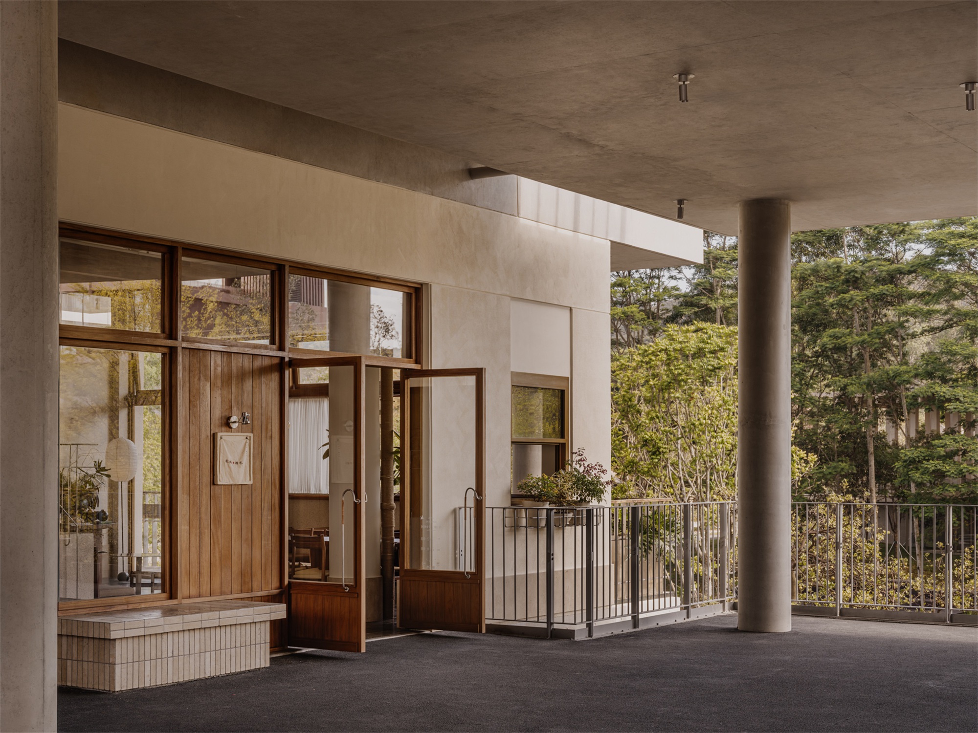 Covered entry portico with cylindrical concrete columns framing timber-framed glazed storefront and planted terrace beyond