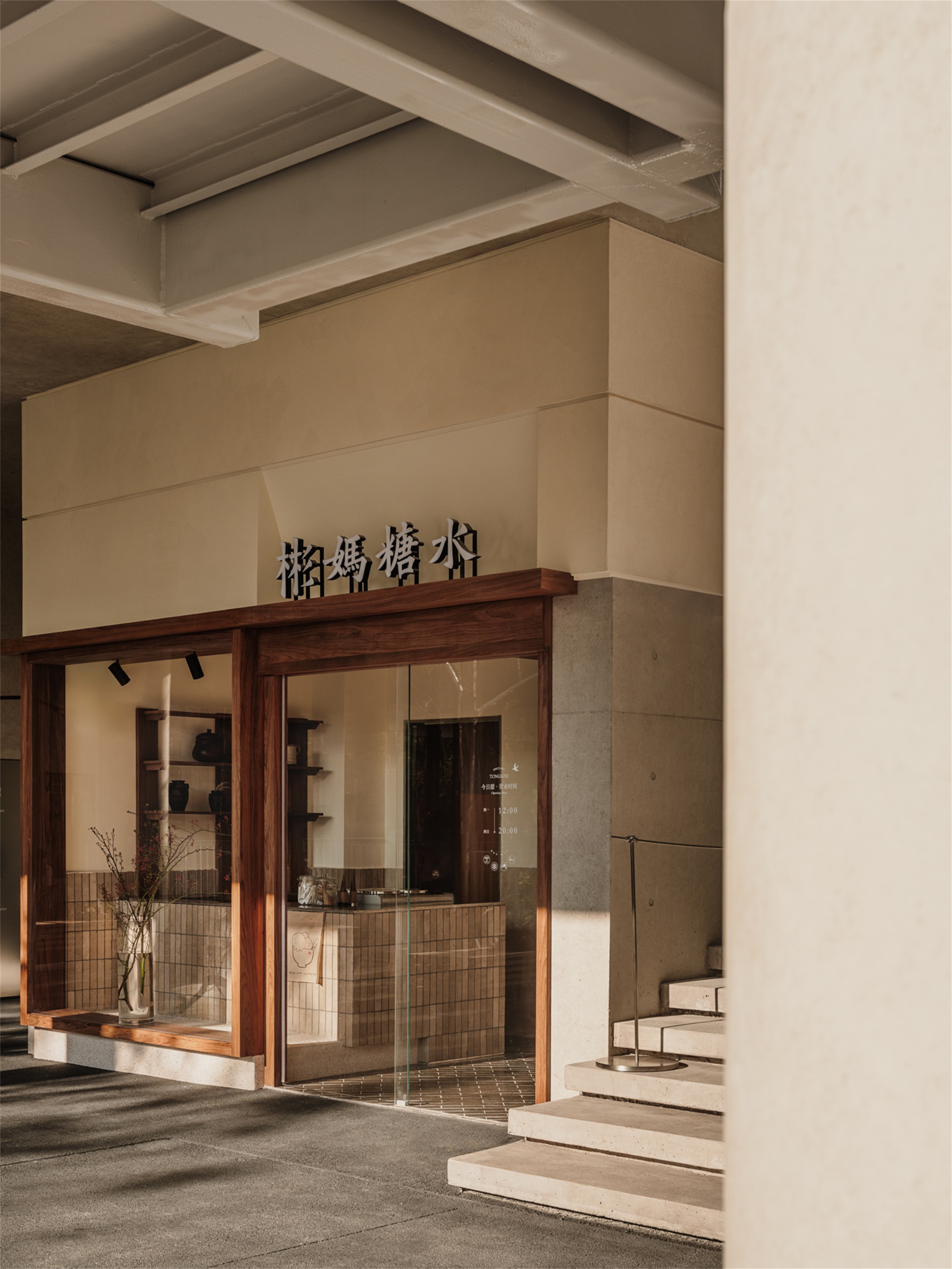Storefront entrance with timber frame, tiled base, and stepped stone pavement under exposed concrete soffit