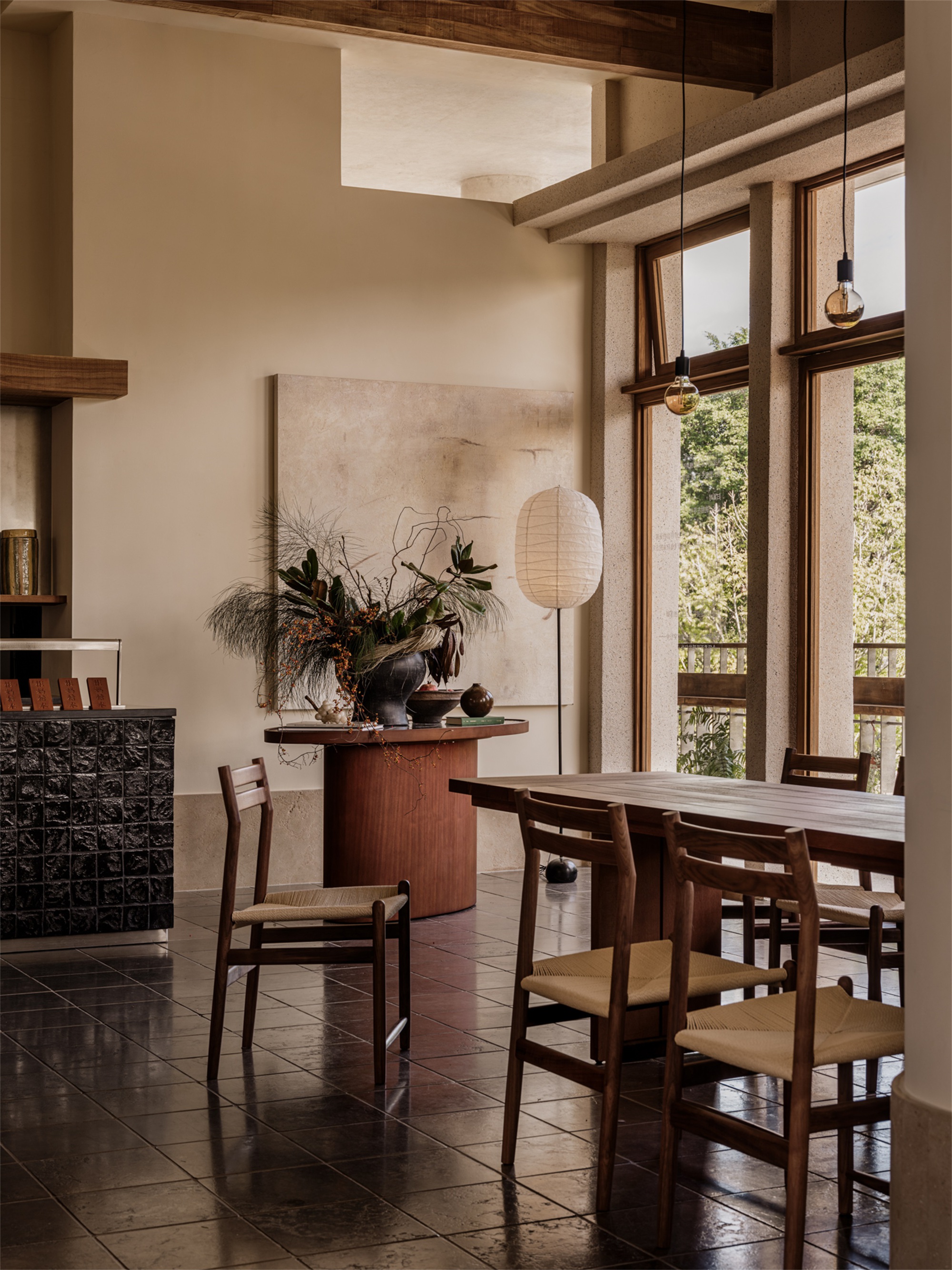 Double-height dining area with exposed timber beams and full-height glazing overlooking greenery