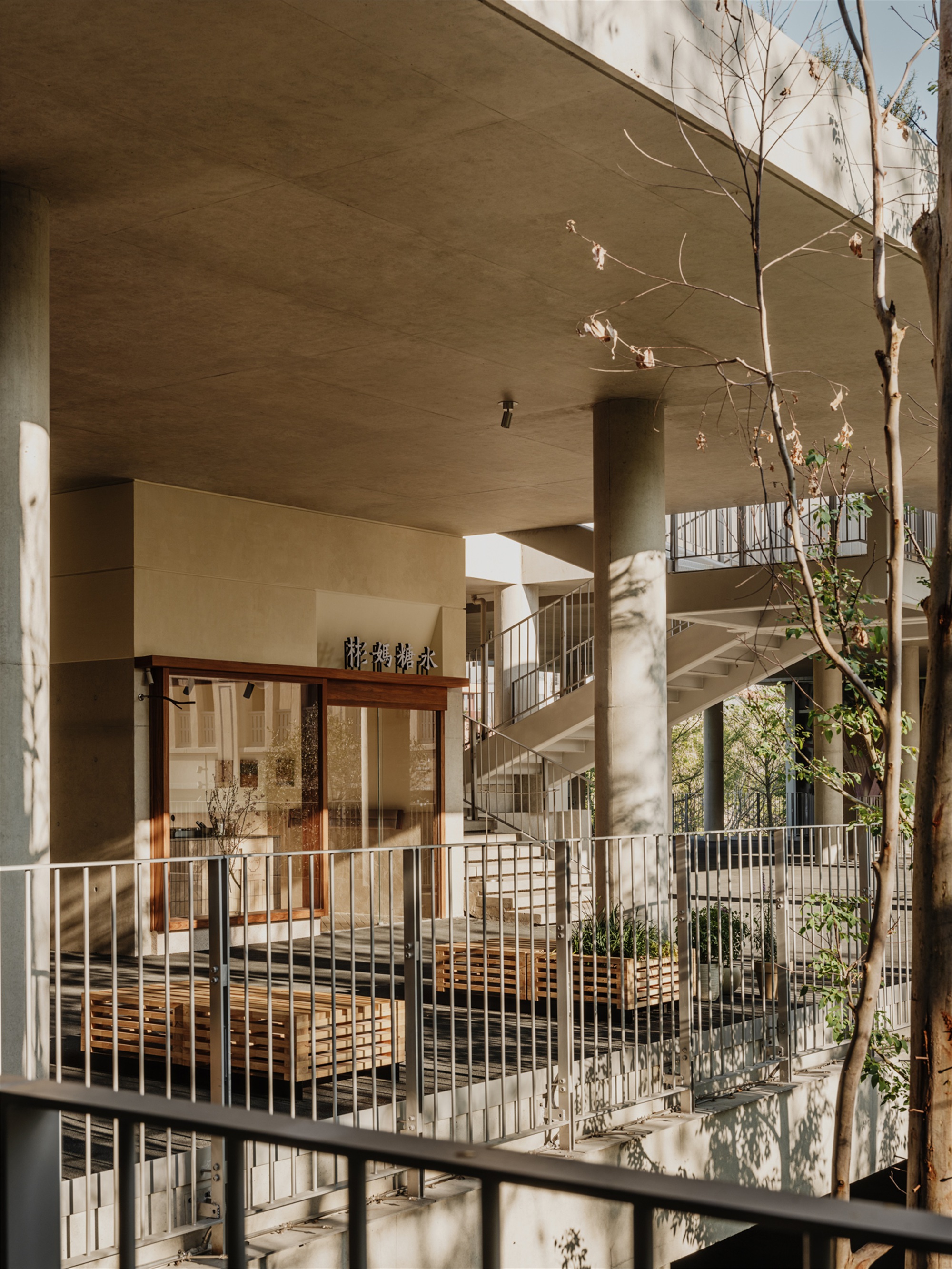 Interior courtyard with cylindrical columns, metal railings, planted balconies, and dappled sunlight through bare branches