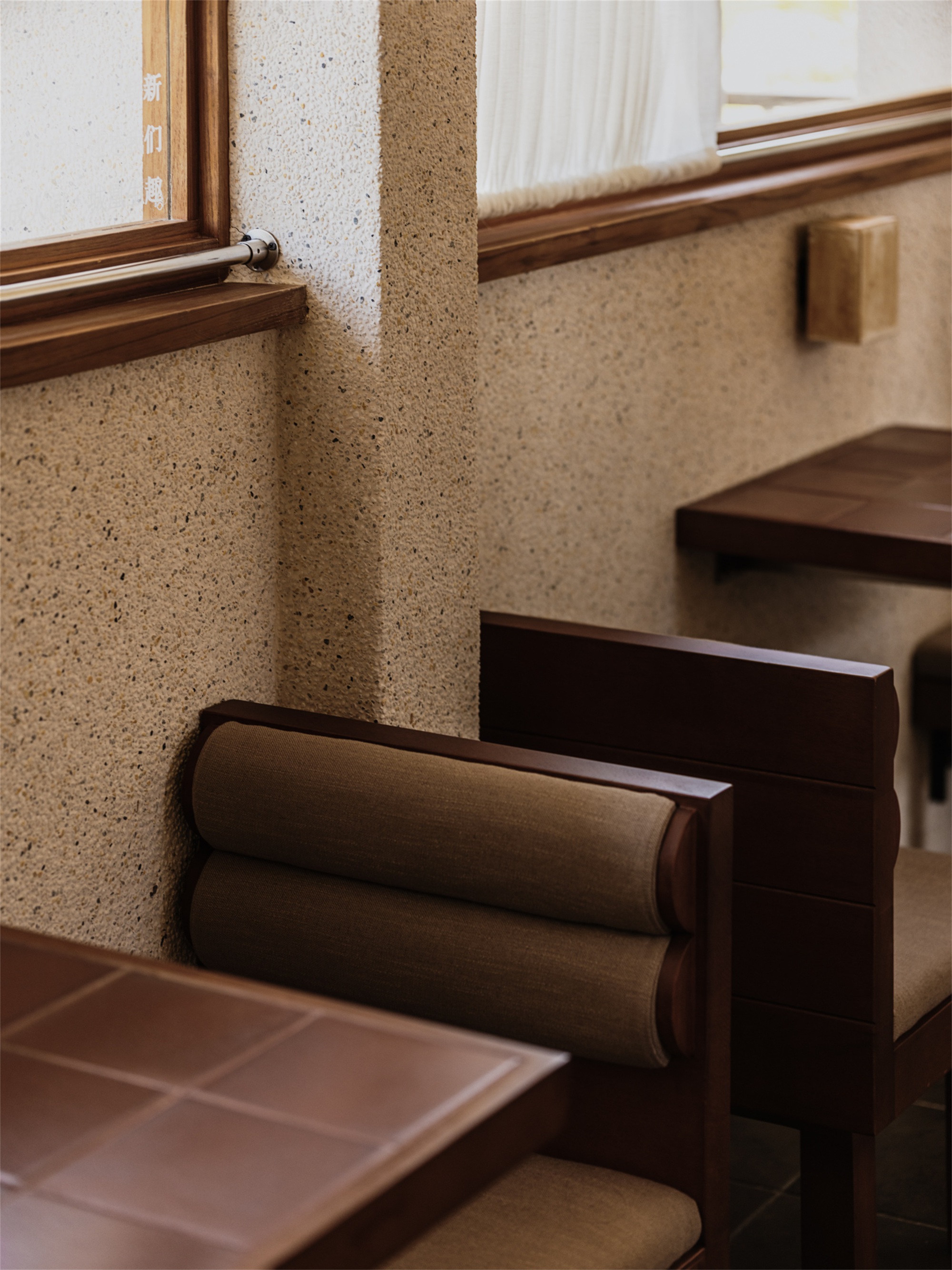 Timber window sill and terrazzo wall meeting a built-in bench with cylindrical bolster cushions