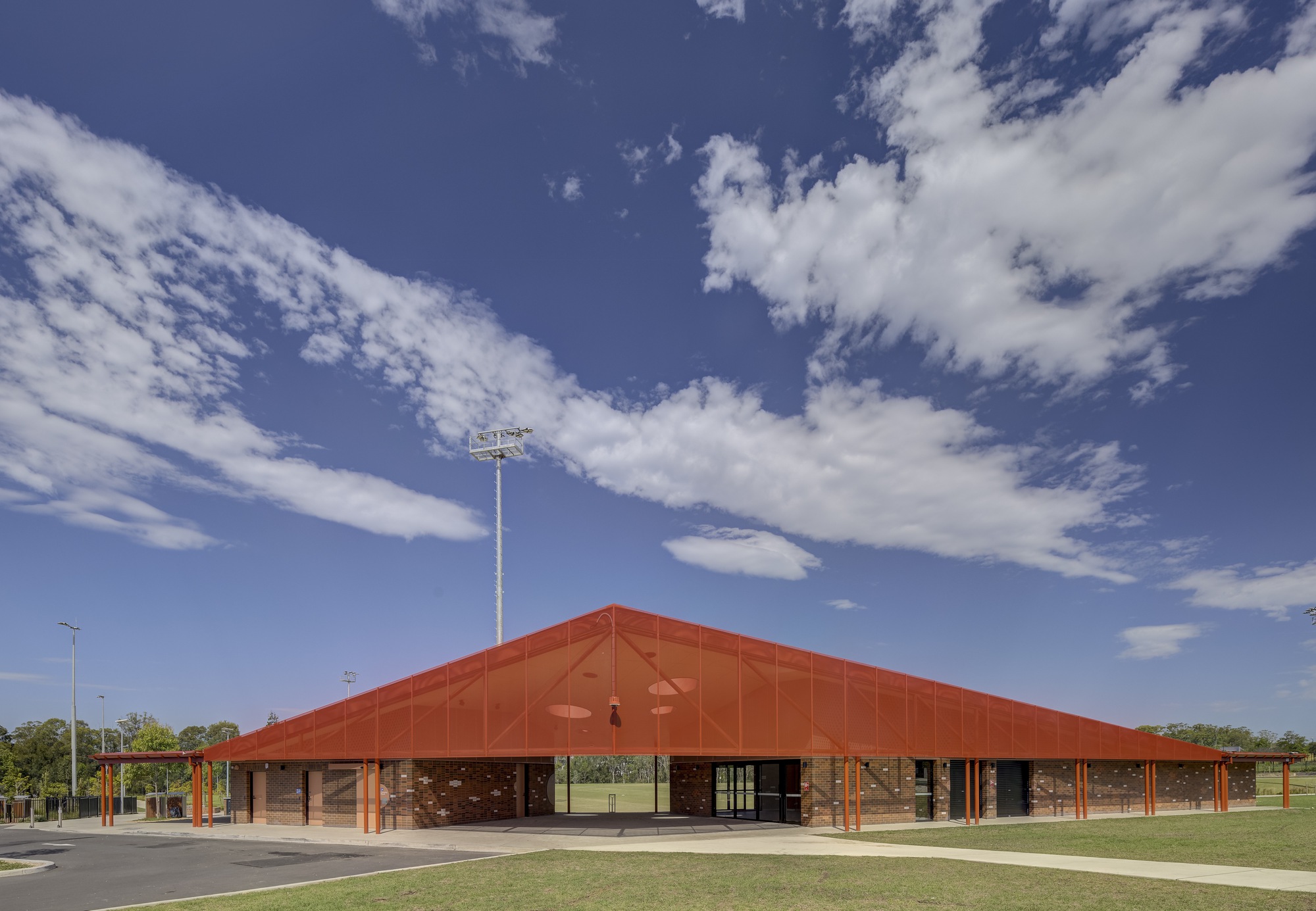 Wide view of the low-pitched terracotta roof pavilion set against playing fields under scattered clouds