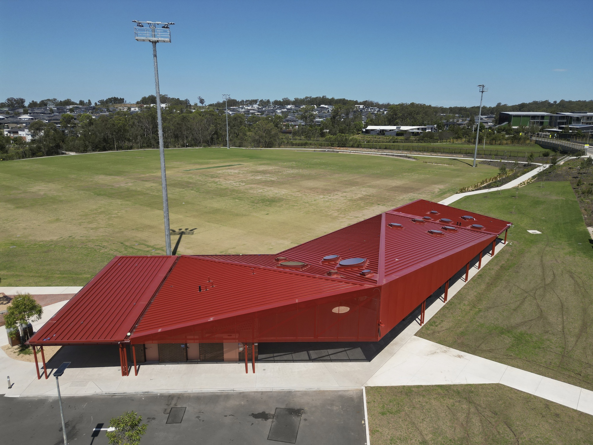 Aerial view of the angular red metal roof with service penetrations beside the oval field