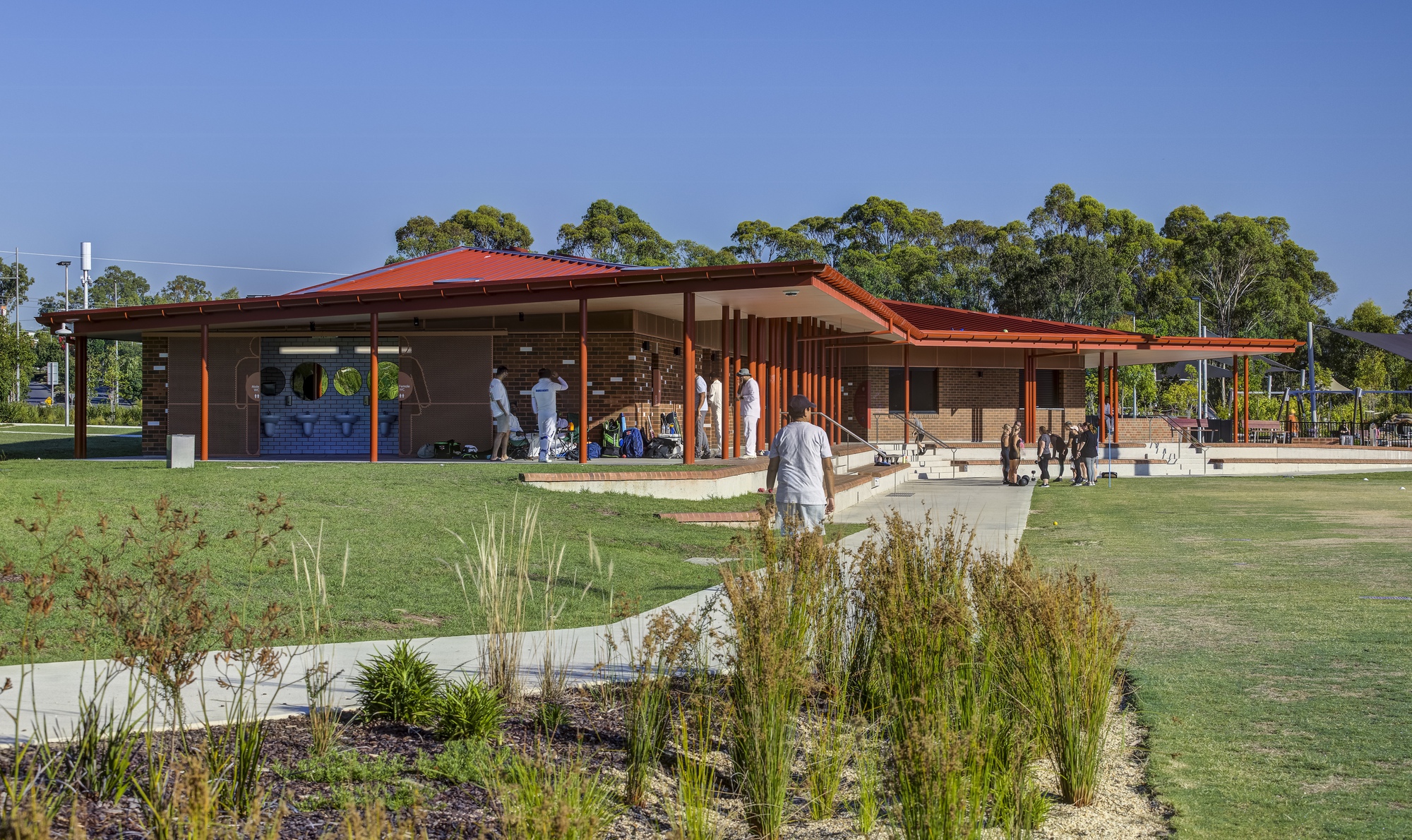 Garden approach with native grasses in the foreground and families walking beneath the wide eaves